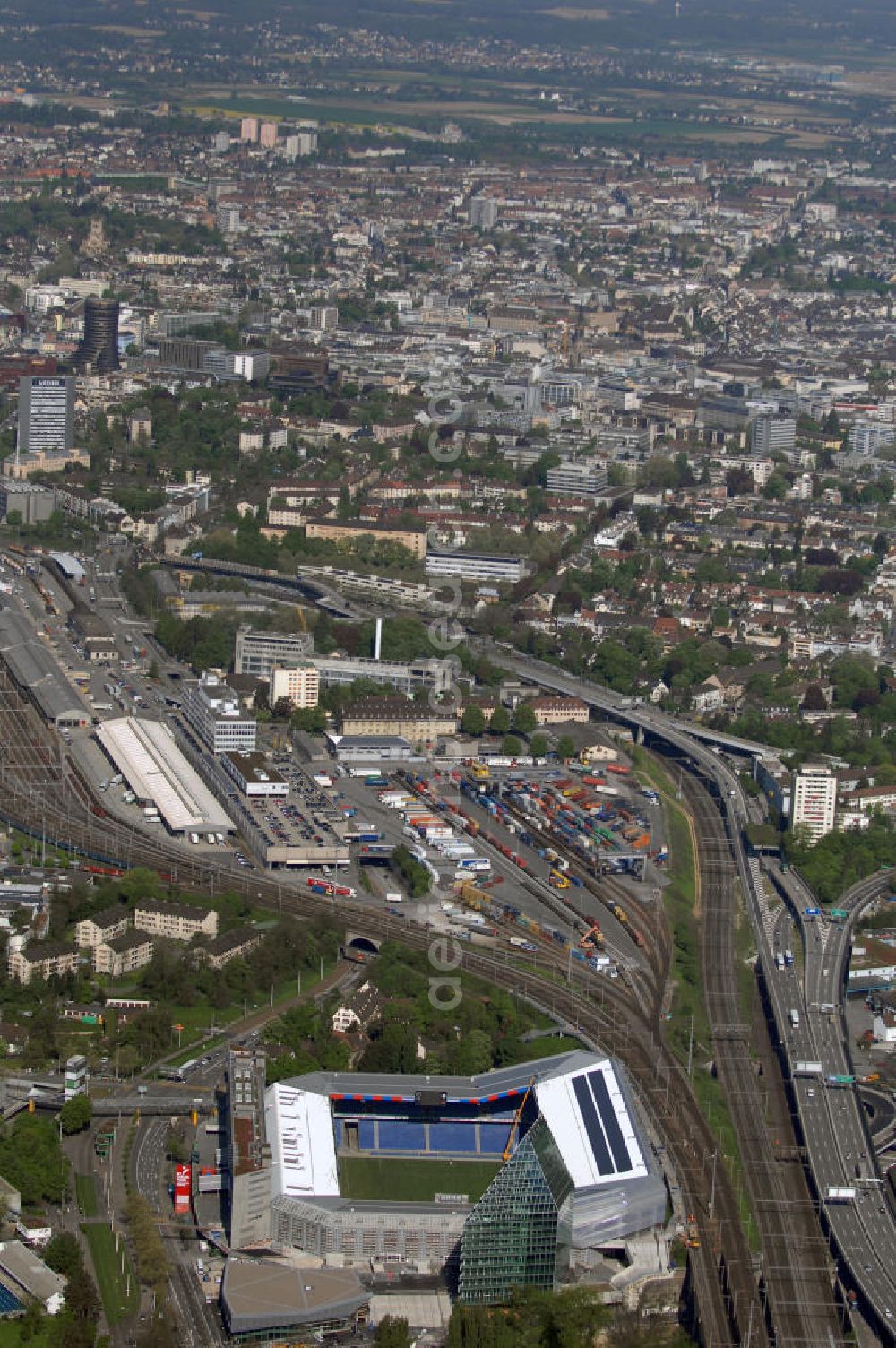 Basel from above - Blick über die Stadt mit Stadion und Bahnhof. Der St. Jakob-Park (früher St. Jakob-Stadion, lokal Joggeli genannt) ist zur Zeit das grösste Fussballstadion der Schweiz und ist Teil des Sportzentrum St. Jakob. Es ist das Heimstadion des Fussballclub Basel (FCB). Es wurde von den Architekten Herzog & de Meuron von 1999 bis 2001 erstellt und hat ein Fassungsvermögen von 38500 Sitzplätzen. Es ist Austragungsort und Eröffnungsort der Europameisterschaft 2008. Zum St. Jakob-Park gehört auch der neu erbaute St.Jakob Turm mit Glasfassade.