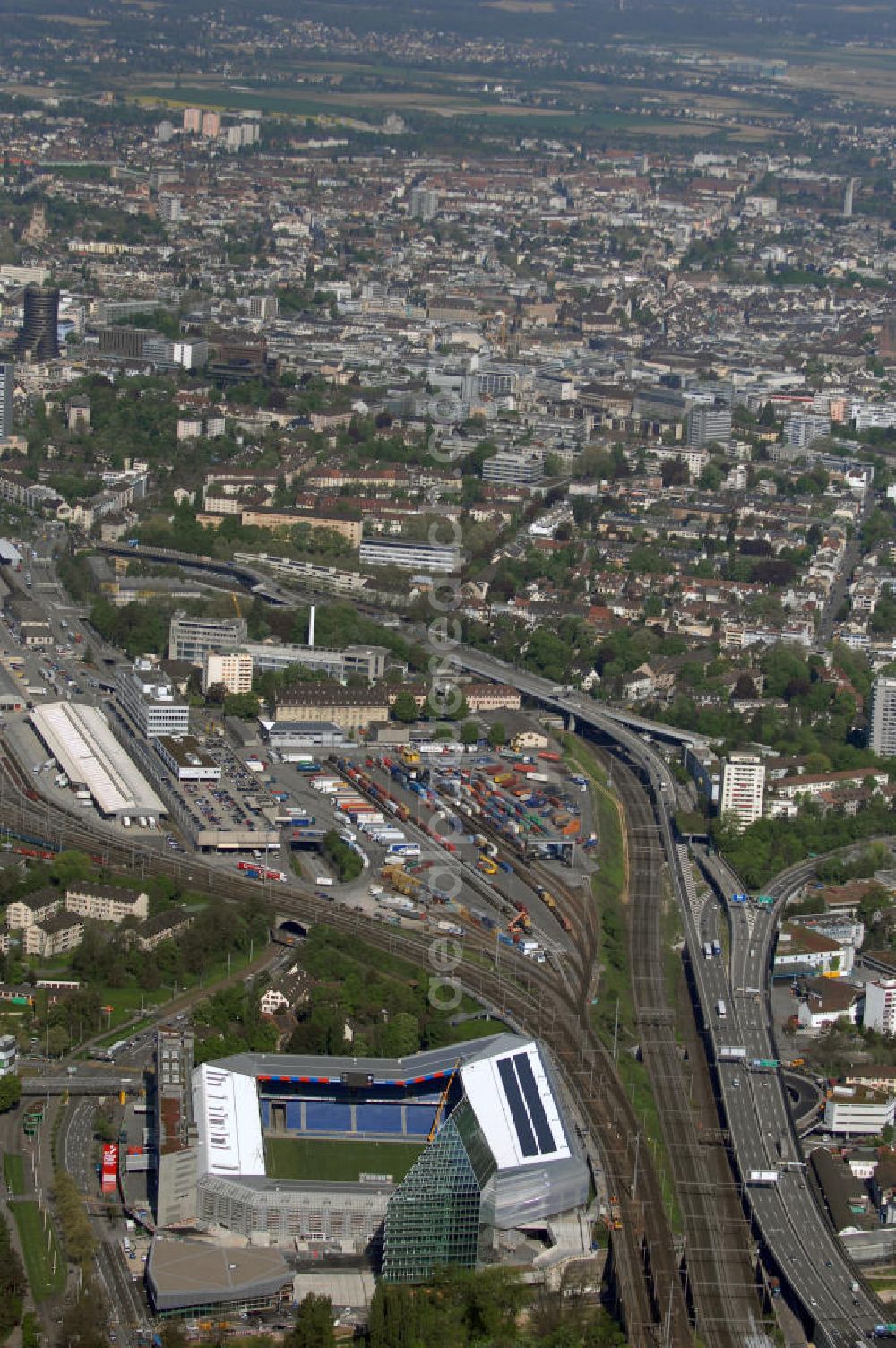 Basel from the bird's eye view: Blick über die Stadt mit Stadion und Bahnhof. Der St. Jakob-Park (früher St. Jakob-Stadion, lokal Joggeli genannt) ist zur Zeit das grösste Fussballstadion der Schweiz und ist Teil des Sportzentrum St. Jakob. Es ist das Heimstadion des Fussballclub Basel (FCB). Es wurde von den Architekten Herzog & de Meuron von 1999 bis 2001 erstellt und hat ein Fassungsvermögen von 38500 Sitzplätzen. Es ist Austragungsort und Eröffnungsort der Europameisterschaft 2008. Zum St. Jakob-Park gehört auch der neu erbaute St.Jakob Turm mit Glasfassade.