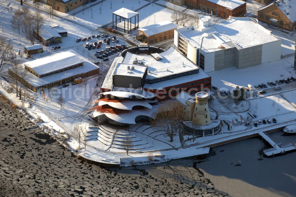 Aerial image POTSDAM - Blick auf das verschneite Hans Otto Theater, dem Brandenburgischen Landestheaters in Potsdam. Seit dem 22. September 2006 spielt das Ensemble in dem neuen Potsdamer Theaterhaus in der Schiffbauergasse am Ufer des Tiefen Sees.Der Architekt Gottfried Böhm entwarf ein fünfgeschossiges Theatergebäude mit schalenförmigen Dächern nach dem Vorbild des Sydney Opera House, die wie drei große Hutkrempen weit in das Ufer der Havel hineinzuragen scheinen. Ein alter Gasometer, der von einer Gasanstalt übrig geblieben ist, ist in die Architektur integriert und dient jetzt als Hof mit Wirtschaftsräumen. Beton und Glas sind die Materialien, die das Bauwerk charakterisieren.Das Obere Foyer und der Bühnensaal haben jeweils eine große Glasfensterfront, die der Bühne kann komplett abgedunkelt werden. Im Großen Saal ist für max. 480 Zuschauer Platz. Unter den Zuschauerreihen sind 50 Hubpodien angeordnet, mit denen das Auditorium gesenkt und gehoben werden kann. Die Hinterbühnen lassen sich weit öffnen, so dass man bis hinaus in den Innenraum des Gasometers schauen kann. BATEG Ingenieurbau GmbH - http://