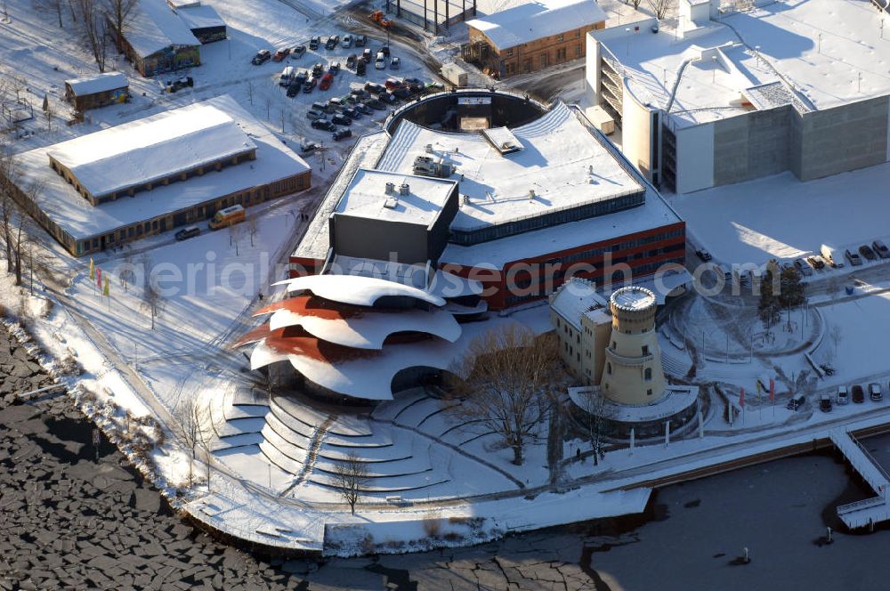 Aerial photograph POTSDAM - Blick auf das verschneite Hans Otto Theater, dem Brandenburgischen Landestheaters in Potsdam. Seit dem 22. September 2006 spielt das Ensemble in dem neuen Potsdamer Theaterhaus in der Schiffbauergasse am Ufer des Tiefen Sees.Der Architekt Gottfried Böhm entwarf ein fünfgeschossiges Theatergebäude mit schalenförmigen Dächern nach dem Vorbild des Sydney Opera House, die wie drei große Hutkrempen weit in das Ufer der Havel hineinzuragen scheinen. Ein alter Gasometer, der von einer Gasanstalt übrig geblieben ist, ist in die Architektur integriert und dient jetzt als Hof mit Wirtschaftsräumen. Beton und Glas sind die Materialien, die das Bauwerk charakterisieren.Das Obere Foyer und der Bühnensaal haben jeweils eine große Glasfensterfront, die der Bühne kann komplett abgedunkelt werden. Im Großen Saal ist für max. 480 Zuschauer Platz. Unter den Zuschauerreihen sind 50 Hubpodien angeordnet, mit denen das Auditorium gesenkt und gehoben werden kann. Die Hinterbühnen lassen sich weit öffnen, so dass man bis hinaus in den Innenraum des Gasometers schauen kann. BATEG Ingenieurbau GmbH - http://