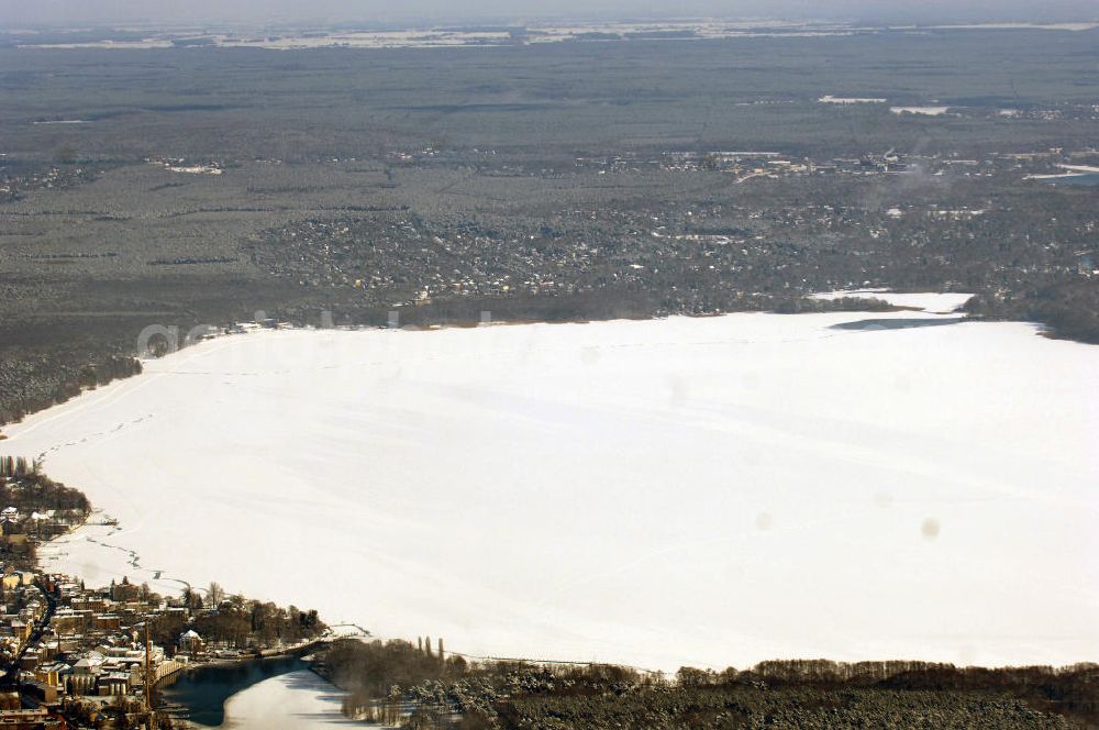 Aerial photograph Berlin - Blick auf das winterlich verschneite Areal des zugefrorenen Müggelsees. Der Müggelsee ist der größte der Berliner Seen. Zur Abgrenzung von dem mit ihm verbundenen, nur etwa 0,16 km² bedeckenden Kleinen Müggelsee wird er als Großer Müggelsee bezeichnet. Der Müggelsee gehört zum Berliner Bezirk Treptow-Köpenick, die Ortsteile Köpenick, Friedrichshagen, Rahnsdorf und Müggelheim grenzen an den See. Der See dehnt sich über 7,4 km² aus (max. 4,3 km lang; 2,6 km breit) und ist bis zu 8 Meter tief. Der See und die am Südrand gelegenen Müggelberge, mit 115 m die höchsten Berliner Erhebungen, entstanden während des Pleistozäns.