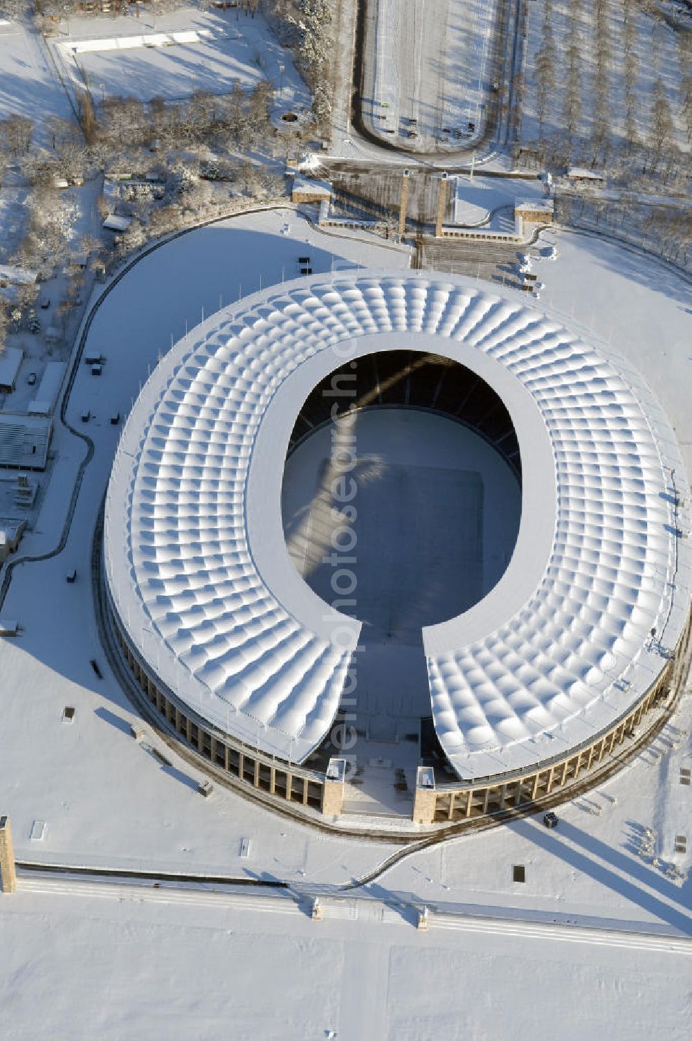 Berlin from above - Blick auf das winterlich verschneite Olypiastadion Berlin. Das Olympiastadion wurde von 1934 bis 1936 anlässlich der Olympischen Sommerspiele 1936 mit einem Fassungsvermögen von 100.000 Zuschauern nach Plänen des Architekten Werner March erbaut.Seine Heimspiele trägt der Hauptnutzer, die Fußball-Bundesliga-Mannschaft von Hertha BSC, im Olympiastadion aus, und die jährlichen Endspiele um den DFB-Pokal der Damen und Herren finden hier seit 1985 statt. Das American-Football-Team von Berlin Thunder bestritt hier seine Heimspiele in der NFL Europe bis Juni 2007. Zusätzlich werden Leichtathletik-Wettkämpfe, wie das jährliche ISTAF, ausgetragen. Am 4. Dezember 2004 wurde Berlin zum Austragungsort der Leichtathletik-Weltmeisterschaft 2009 erkoren, die im Olympiastadion ausgetragen werden wird. Gelegentlich wird das Stadion auch für Großveranstaltungen ohne sportlichen Charakter, wie etwa Kirchentage oder Konzerte, genutzt. Das Olympiastadion besitzt die größte Stadionkapelle der Welt. http://