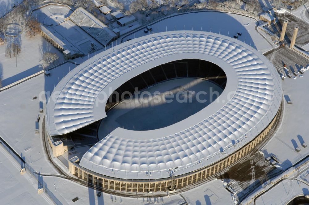 Berlin from the bird's eye view: Blick auf das winterlich verschneite Olypiastadion Berlin. Das Olympiastadion wurde von 1934 bis 1936 anlässlich der Olympischen Sommerspiele 1936 mit einem Fassungsvermögen von 100.000 Zuschauern nach Plänen des Architekten Werner March erbaut.Seine Heimspiele trägt der Hauptnutzer, die Fußball-Bundesliga-Mannschaft von Hertha BSC, im Olympiastadion aus, und die jährlichen Endspiele um den DFB-Pokal der Damen und Herren finden hier seit 1985 statt. Das American-Football-Team von Berlin Thunder bestritt hier seine Heimspiele in der NFL Europe bis Juni 2007. Zusätzlich werden Leichtathletik-Wettkämpfe, wie das jährliche ISTAF, ausgetragen. Am 4. Dezember 2004 wurde Berlin zum Austragungsort der Leichtathletik-Weltmeisterschaft 2009 erkoren, die im Olympiastadion ausgetragen werden wird. Gelegentlich wird das Stadion auch für Großveranstaltungen ohne sportlichen Charakter, wie etwa Kirchentage oder Konzerte, genutzt. Das Olympiastadion besitzt die größte Stadionkapelle der Welt. http://