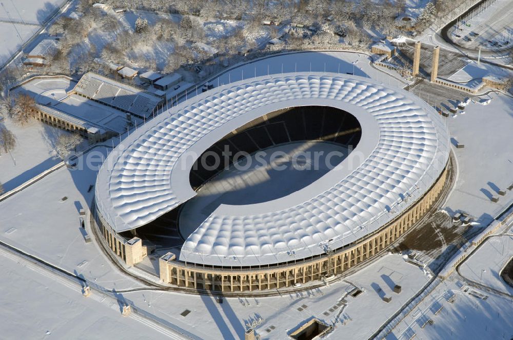 Berlin from above - Blick auf das winterlich verschneite Olypiastadion Berlin. Das Olympiastadion wurde von 1934 bis 1936 anlässlich der Olympischen Sommerspiele 1936 mit einem Fassungsvermögen von 100.000 Zuschauern nach Plänen des Architekten Werner March erbaut.Seine Heimspiele trägt der Hauptnutzer, die Fußball-Bundesliga-Mannschaft von Hertha BSC, im Olympiastadion aus, und die jährlichen Endspiele um den DFB-Pokal der Damen und Herren finden hier seit 1985 statt. Das American-Football-Team von Berlin Thunder bestritt hier seine Heimspiele in der NFL Europe bis Juni 2007. Zusätzlich werden Leichtathletik-Wettkämpfe, wie das jährliche ISTAF, ausgetragen. Am 4. Dezember 2004 wurde Berlin zum Austragungsort der Leichtathletik-Weltmeisterschaft 2009 erkoren, die im Olympiastadion ausgetragen werden wird. Gelegentlich wird das Stadion auch für Großveranstaltungen ohne sportlichen Charakter, wie etwa Kirchentage oder Konzerte, genutzt. Das Olympiastadion besitzt die größte Stadionkapelle der Welt. http://