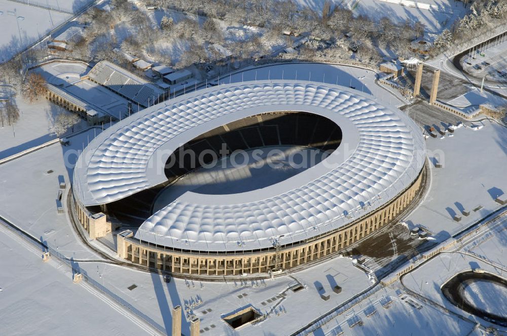 Berlin from the bird's eye view: Blick auf das winterlich verschneite Olypiastadion Berlin. Das Olympiastadion wurde von 1934 bis 1936 anlässlich der Olympischen Sommerspiele 1936 mit einem Fassungsvermögen von 100.000 Zuschauern nach Plänen des Architekten Werner March erbaut.Seine Heimspiele trägt der Hauptnutzer, die Fußball-Bundesliga-Mannschaft von Hertha BSC, im Olympiastadion aus, und die jährlichen Endspiele um den DFB-Pokal der Damen und Herren finden hier seit 1985 statt. Das American-Football-Team von Berlin Thunder bestritt hier seine Heimspiele in der NFL Europe bis Juni 2007. Zusätzlich werden Leichtathletik-Wettkämpfe, wie das jährliche ISTAF, ausgetragen. Am 4. Dezember 2004 wurde Berlin zum Austragungsort der Leichtathletik-Weltmeisterschaft 2009 erkoren, die im Olympiastadion ausgetragen werden wird. Gelegentlich wird das Stadion auch für Großveranstaltungen ohne sportlichen Charakter, wie etwa Kirchentage oder Konzerte, genutzt. Das Olympiastadion besitzt die größte Stadionkapelle der Welt. http://