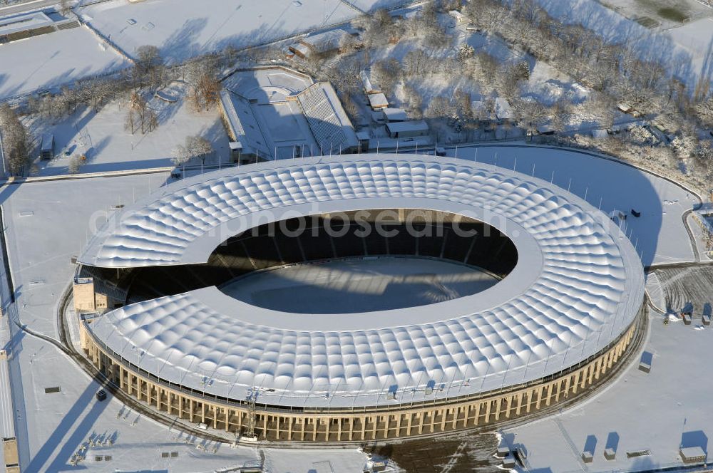 Aerial photograph Berlin - Blick auf das winterlich verschneite Olypiastadion Berlin. Das Olympiastadion wurde von 1934 bis 1936 anlässlich der Olympischen Sommerspiele 1936 mit einem Fassungsvermögen von 100.000 Zuschauern nach Plänen des Architekten Werner March erbaut.Seine Heimspiele trägt der Hauptnutzer, die Fußball-Bundesliga-Mannschaft von Hertha BSC, im Olympiastadion aus, und die jährlichen Endspiele um den DFB-Pokal der Damen und Herren finden hier seit 1985 statt. Das American-Football-Team von Berlin Thunder bestritt hier seine Heimspiele in der NFL Europe bis Juni 2007. Zusätzlich werden Leichtathletik-Wettkämpfe, wie das jährliche ISTAF, ausgetragen. Am 4. Dezember 2004 wurde Berlin zum Austragungsort der Leichtathletik-Weltmeisterschaft 2009 erkoren, die im Olympiastadion ausgetragen werden wird. Gelegentlich wird das Stadion auch für Großveranstaltungen ohne sportlichen Charakter, wie etwa Kirchentage oder Konzerte, genutzt. Das Olympiastadion besitzt die größte Stadionkapelle der Welt. http://