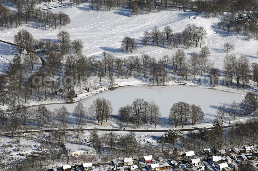 Aerial photograph Berlin - Blick auf die winterlich verschneiten Britzer Garten.Der Britzer Garten, benannt nach dem Berliner Ortsteil Britz, wurde für die Bundesgartenschau 1985 angelegt, um der damals vom Umland abgeschnittenen Bevölkerung im Süden West-Berlins einen neuen Landschaftspark zu bieten.Der Britzer Garten wurde auf Ackerflächen und Kleingartenkolonien angelegt; weitestgehend wurden jedoch vorhandene Kleingartenkolonien erhalten. Er befindet sich am südwestlichen Rand des damaligen Berliner Bezirkes Neukölln und grenzt an den Bezirk Tempelhof mit dem Ortsteil Mariendorf an. Er wird durch die Hauptstraßenachsen Mariendorfer Damm, Mohriner Allee, Buckower Damm und Alt-Buckow / Marienfelder Allee eingerahmt. Am Rand dieser Hauptstraßen befindet sich meist offene Wohnbebauung. Noch im Eröffnungsjahr 1985 bestand die planerische Absicht, eine Verlängerung der Berliner Stadtautobahn von der Anschlussstelle Gradestraße durch das Gartengelände hindurch bis zur Berliner Stadtgrenze zu bauen, um dort einen neuen Grenzübergang mit Weiterführung zum Berliner Ring einrichten zu können.