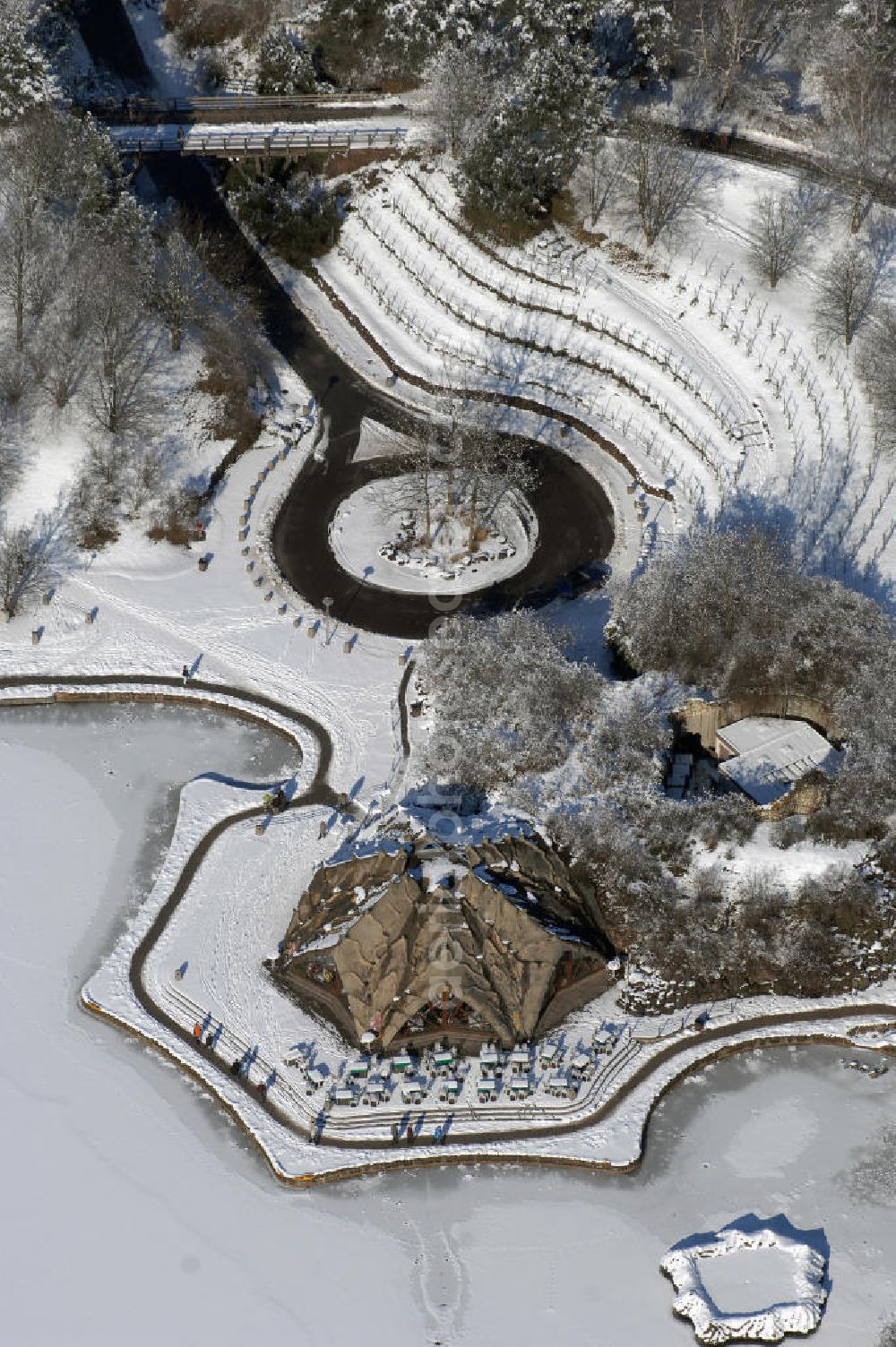 Berlin from above - Blick auf die winterlich verschneiten Britzer Garten.Der Britzer Garten, benannt nach dem Berliner Ortsteil Britz, wurde für die Bundesgartenschau 1985 angelegt, um der damals vom Umland abgeschnittenen Bevölkerung im Süden West-Berlins einen neuen Landschaftspark zu bieten.Der Britzer Garten wurde auf Ackerflächen und Kleingartenkolonien angelegt; weitestgehend wurden jedoch vorhandene Kleingartenkolonien erhalten. Er befindet sich am südwestlichen Rand des damaligen Berliner Bezirkes Neukölln und grenzt an den Bezirk Tempelhof mit dem Ortsteil Mariendorf an. Er wird durch die Hauptstraßenachsen Mariendorfer Damm, Mohriner Allee, Buckower Damm und Alt-Buckow / Marienfelder Allee eingerahmt. Am Rand dieser Hauptstraßen befindet sich meist offene Wohnbebauung. Noch im Eröffnungsjahr 1985 bestand die planerische Absicht, eine Verlängerung der Berliner Stadtautobahn von der Anschlussstelle Gradestraße durch das Gartengelände hindurch bis zur Berliner Stadtgrenze zu bauen, um dort einen neuen Grenzübergang mit Weiterführung zum Berliner Ring einrichten zu können.