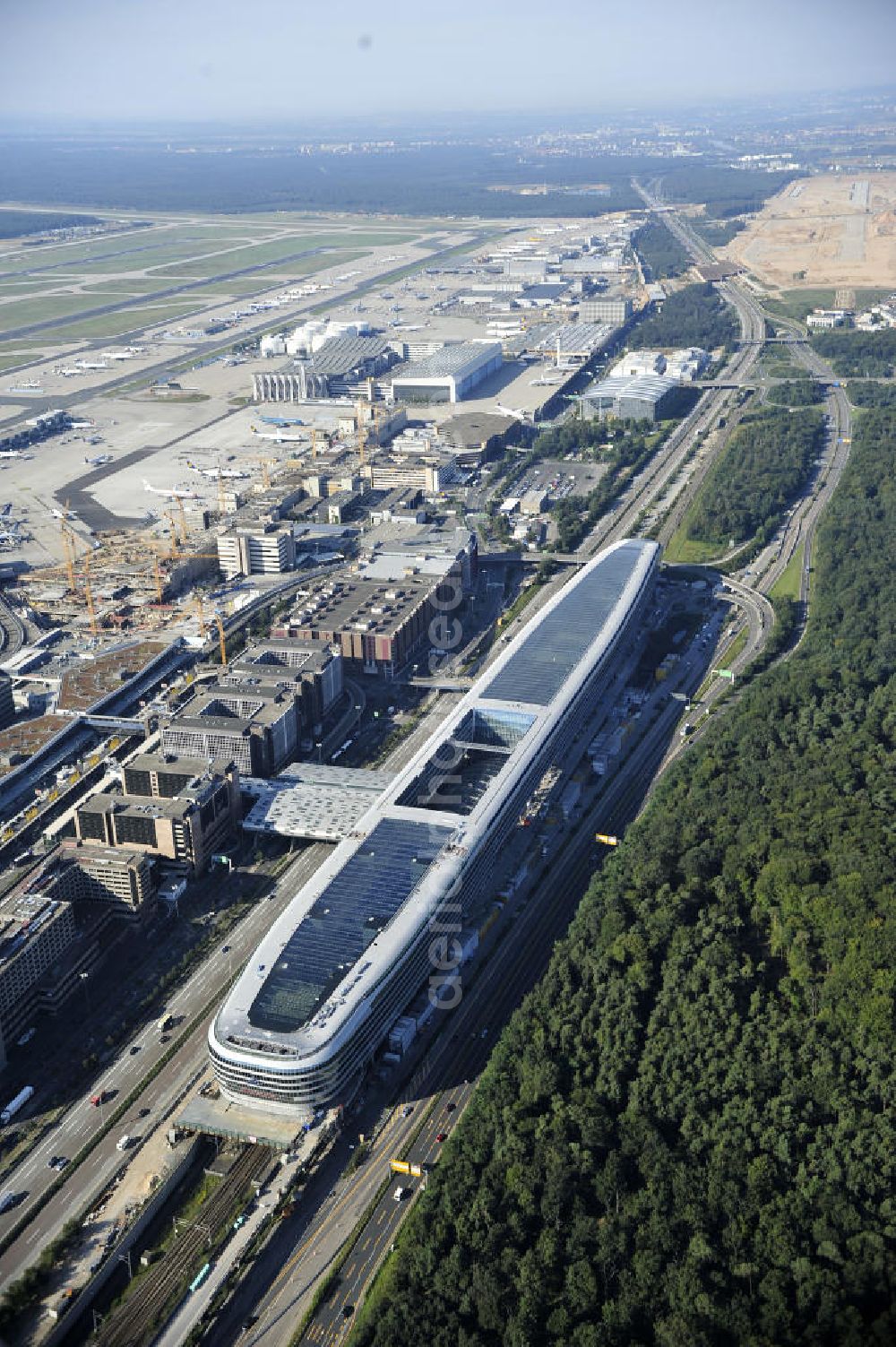 Aerial photograph Frankfurt am Main - Blick auf das Businesscenter The Squaire, vormals als Airrail Center Frankfurt bekannt. Hauptinvestor für das futuristische Projekt ist die IVG Immobilien AG. Das 660 Meter lange und neun Etagen (45 Meter) hohe Gebäude wurde über dem Fernbahnhof gebaut, um eine zusätzliche Fläche für Büros, Hotels und Einkaufszentren zu bieten. Das u.a. mit der Streif Baulogistik GmbH errichtete Bauwerk ist auf die Decke des Fernbahnhofs gesetzt, die wie die Pfeiler des Grundbauwerks bereits entsprechend ausgelegt wurde. Das Center ist somit direkt mit dem Terminal 1 und dem Fernbahnhof verbunden. View of the Business Center The Squair, formerly known as Airrail Center Frankfurt. The main investor for the futuristic project is the IVG Immobilien AG.