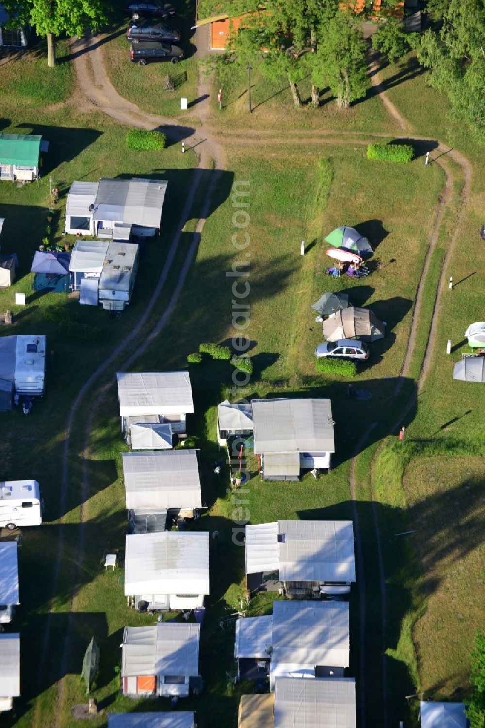 Aerial photograph Neuruppin - Camping with caravans on the lakeside of Zermuetzelsee in Neuruppin in the state of Brandenburg. Neuruppin is the main town of the Ruppiner Land region and capital of the county district of Ostprignitz-Ruppin in the North of the state. The lake is located in the North of the town in the Ruppiner Switzerland region and is surrounded by forest. The white caravans are standing on the lakeside