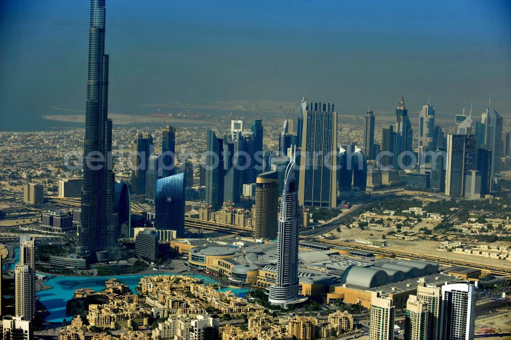 DUBAI / DUBAYY from above - Blick auf das Burj Khalifa in der Skyline von Dubai, dem derzeit höchsten Gebäude der Welt. Das Hochhaus wurde von der Projektgesellschaft Emaar Properties nach Plänen des Architekten Adrian Smith vom amerikanischen Architekturbüro Skidmore, Owings and Merrill gebaut. Das Hochhaus ist Mittelpunkt von Downtown Dubai, eines neuen Stadtentwicklungsgebietes.Rechts die Dubai Mall, das derzeit zweitgrößtem Einkaufszentrum der Welt. Die Dubai Mall wurde konzipiert von Emaar Properties in einem Areal von Apartment- und Bürogebäuden, zahlreiche Hotels und eine neu gebaute, arabisch wirkende Altstadt mit Wasserbeckenlandschaft und der weltgrößten Springbrunnenanlage. Aerial view of the Burj Khalifa and the shopping mall Dubai Mall, currently the second largest shopping center in the world in the new Downtown Dubai district.