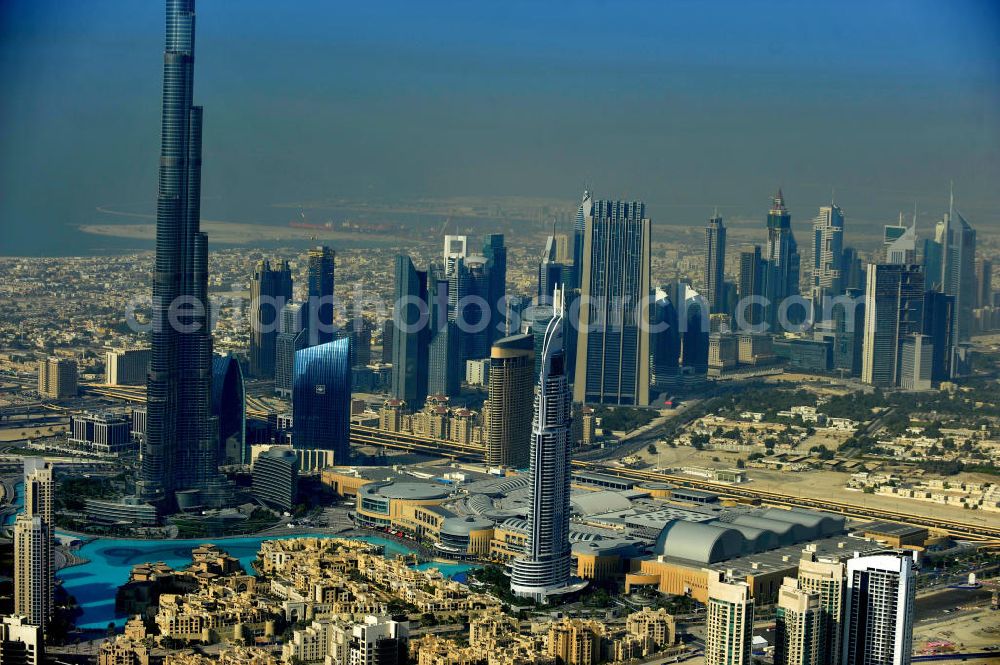 DUBAI / DUBAYY from the bird's eye view: Blick auf das Burj Khalifa in der Skyline von Dubai, dem derzeit höchsten Gebäude der Welt. Das Hochhaus wurde von der Projektgesellschaft Emaar Properties nach Plänen des Architekten Adrian Smith vom amerikanischen Architekturbüro Skidmore, Owings and Merrill gebaut. Das Hochhaus ist Mittelpunkt von Downtown Dubai, eines neuen Stadtentwicklungsgebietes.Rechts die Dubai Mall, das derzeit zweitgrößtem Einkaufszentrum der Welt. Die Dubai Mall wurde konzipiert von Emaar Properties in einem Areal von Apartment- und Bürogebäuden, zahlreiche Hotels und eine neu gebaute, arabisch wirkende Altstadt mit Wasserbeckenlandschaft und der weltgrößten Springbrunnenanlage. Aerial view of the Burj Khalifa and the shopping mall Dubai Mall, currently the second largest shopping center in the world in the new Downtown Dubai district.