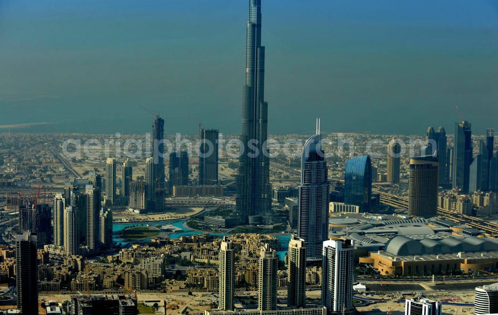 Aerial photograph DUBAI / DUBAYY - Blick auf das Burj Khalifa in der Skyline von Dubai, dem derzeit höchsten Gebäude der Welt. Das Hochhaus wurde von der Projektgesellschaft Emaar Properties nach Plänen des Architekten Adrian Smith vom amerikanischen Architekturbüro Skidmore, Owings and Merrill gebaut. Das Hochhaus ist Mittelpunkt von Downtown Dubai, eines neuen Stadtentwicklungsgebietes. In den unteren 37 der allgemein nutzbaren 163 Etagen ist das weltweit erste Armani-Hotel eingezogen. Einige tausend Tonnen Stahl in den oberen Geschossen sind Recycling-Stahl aus dem abgerissenen Palast der Republik in Berlin. Die Firma Bauer Spezialtiefbau als Subunternehmer bei der Fundamentlegung. Der verarbeitungsfertige flüssige Beton wurde mit Hochleistungsbetonpumpen der Firma Putzmeister auf die jeweilige Arbeitshöhe transportiert. Skyscraper Burj Khalifa, currently the tallest building in the world.