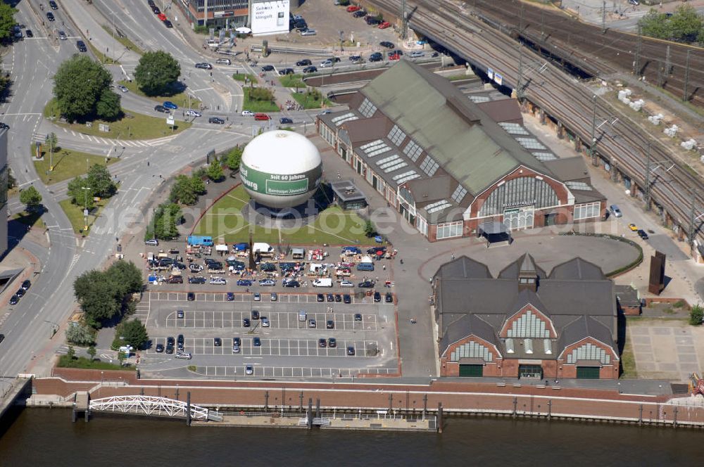 Hamburg from above - Blick auf die Deichtorhallen und den Highflyer Fesselballon. Davor ist ein Flohmarkt aufgebaut. Die Deichtorhallen sind Europas größte Kunstausstellungshallen und gliedern sich in das Haus der Photographie und eine zweite Ausstellungshalle für aktuelle Kunst. Hier finden nicht nur Ausstellungen schon großer und namhafter Künstler statt, auch junge noch unbekannte Künstler bekommen immer wieder die Möglichkeit ihre Werke in einem recht großen Rahmen auszustellen. Neben den Ausstellungsräumen gibt es auch einen Design- und Buchshop der Photographie, sowie ein Restaurant. Zwischen den beiden Gebäuden der Deichtorhallen befindet sich eine weitere Touristenattraktion, der Highflyer Fesselballon. Er ist fest installiert und an einem 180 Meter langen Drahtseil befestigt um immer wieder an der gleichen Stellen landen zu können. Mit ihm können 30 Personen in die Luft steigen und die Aussicht auf und über Hamburg genießen. Kontakt: Deichtorhallen Hamburg GmbH, Deichtorstraße 1-2 20095 Hamburg, Tel. +49(0)40 3210 30,mail@deichtorhallen.de