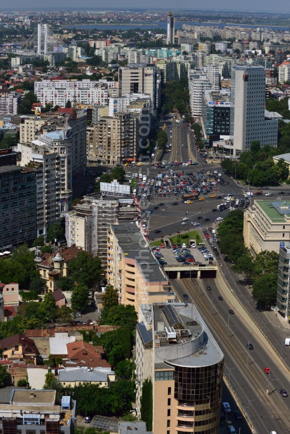 Aerial photograph Bukarest - The Square Piata Victoriei, the Victory Square, in Sector 1 in Bucharest in Romania. View from the Boulevard Iancu de Hunedoara to the West and the large square and traffic junction, where several large roads of the capital meet and intersect. The square itself consists of several parking lots. An underpass leads the traffic and the street car under the central square. On the Victory square, there are several significant buildings such as the Museum of Natural History Antipa which is surrounded by forest, the Bucharest Tower Center and the BRD Tower, which are the highest buildings of the country. The building with the green roof on the East corner of the square is the Victoria Palace, the government seat of Romania which was built during World War II