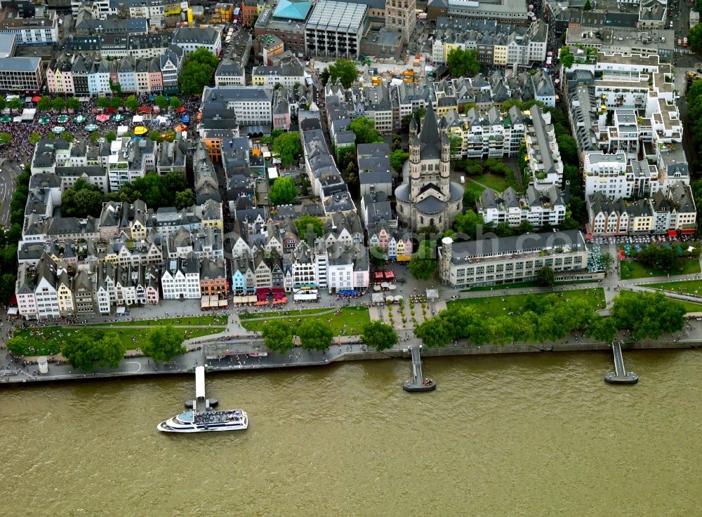 Köln from above - The church Groß St. Martin at the Rhine riverbank in Cologne in the state of North Rhine-Westphalia. The church is one of twelve large romanic churches in the historic city center. It is closely surrounded by history influenced residential and business buildings of the 1970s and 1980s. Large groups of people move through the city center on Christopher Street Day