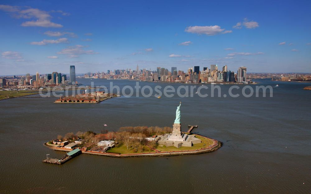 Aerial photograph New York - Die Freiheitsstatue ist eine von Frédéric-Auguste Bartholdi geschaffene neoklassizistische Kolossalstatue bei New York. Sie steht auf Liberty Island im New Yorker Hafen und wurde am 28. Oktober 1886 eingeweiht. Die Statue ist seit 1984 als Weltkulturerbe der UNESCO klassifiziert. Die Statue stellt die in Roben gehüllte Figur der Libertas, der römischen Göttin der Freiheit, dar. / The Statue of Liberty is a statue created by Frédéric-Auguste Bartholdi. It stands on Liberty Iceland in the New York harbor, and was inaugurated in October 1886. The statue has been classified since 1984 as a World Heritage Site by UNESCO. The statue represents the figure of Libertas, the Roman goddess of freedom.