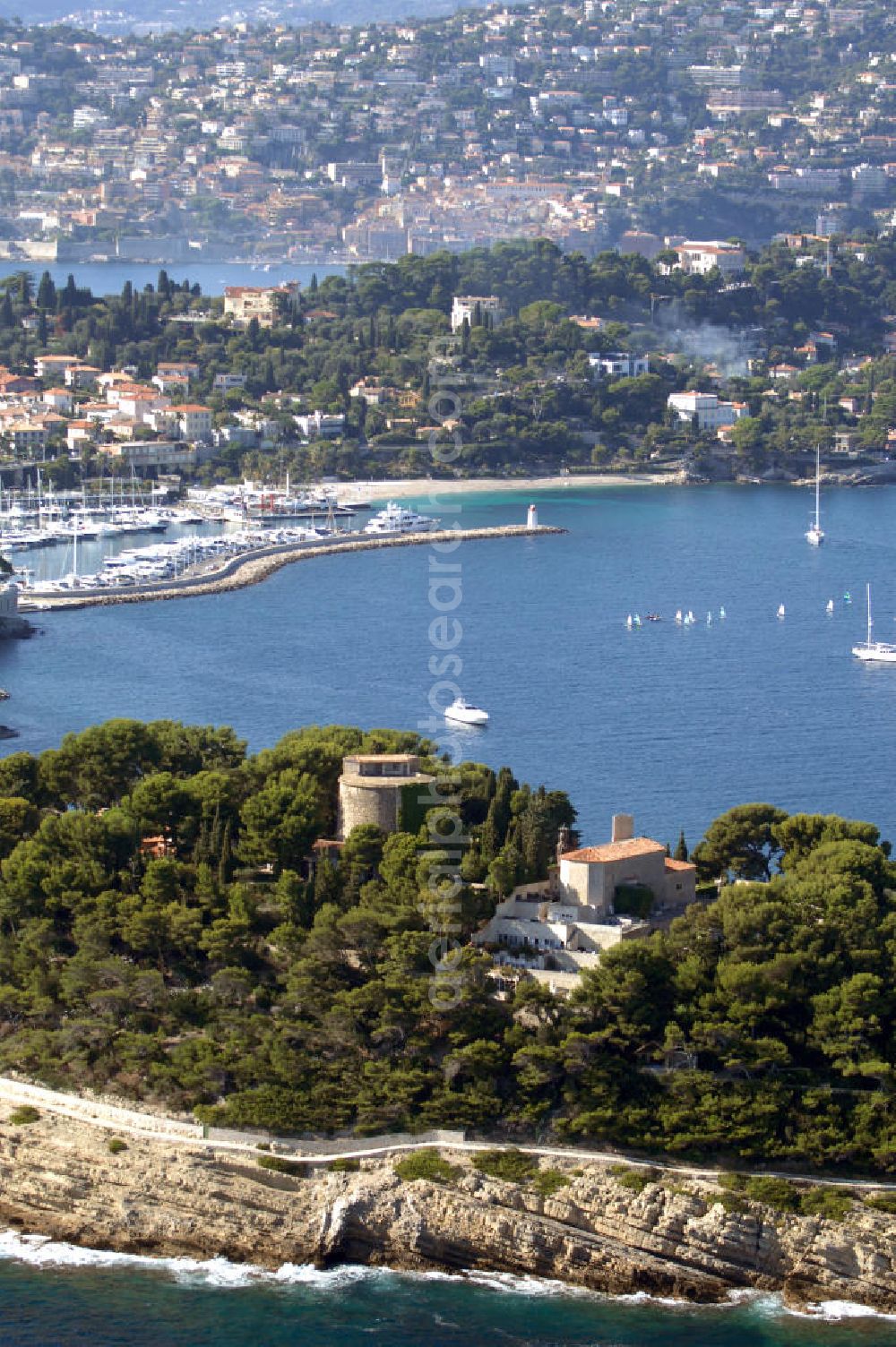 Saint-Jean-Cap-Ferrat from above - Blick auf die Halbinsel Saint-Jean-Cap-Ferrat und den Hafen. Das Cap Ferrat ist eine Halbinsel an der Cote d'Azur. Sie liegt zwischen Nizza und Monaco. Es trennt Beaulieu-sur-Mer und Villefranche-sur-Mer. Der Ort Saint-Jean-Cap-Ferrat erstreckt sich an seinem Ostufer. Die ganze Halbinsel kann auf einem Fußweg umrundet werden. An ihrer Spitze steht ein Leuchtturm als Hafenwegweiser.