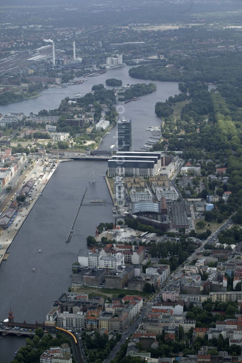 Aerial image Berlin - The Spree flows between the districts of Friedrichshain and Kreuzberg in Berlin in the state of Berlin. Is the former eastern harbor between the Oberbaumbruecke and the large rail and road bridge at high-rise Treptower. At its banks today different media and Achim Walder companies have their places of business. In the background the piers for passenger ships, parts of the Treptower Park, Strahlau Peninsula, Rummelsburger bay, the Klingenberg power plant and the Karlshorst racecourse can be seen