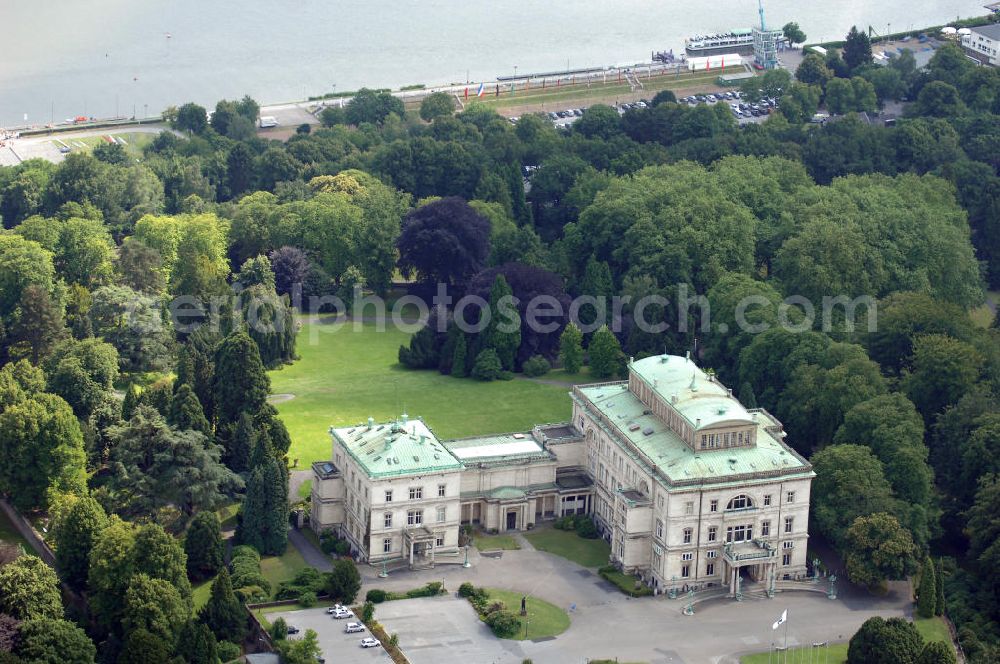 Aerial photograph ESSEN - Die Villa Hügel, im Essener Stadtteil Bredeney gelegen, wurde 1873 von Alfred Krupp errichtet und ist das ehemalige Wohn- und Repräsentationshaus der Industriellenfamilie Krupp. Die Villa hat 269 Räume, 8100 m² Wohn- und Nutzfläche und liegt in einem 28 Hektar großen Park an prominenter Stelle über dem Ruhrtal und dem Baldeneysee. Verwaltet wird sie heute durch die Kulturstiftung Ruhr, welche regelmäßig Veranstaltungen wie Konzerte oder Ausstellungen dort durchführt. Außerhalb dieser Zeiten kann sie in den Öffnungszeiten besichtigt werden.Die Entstehung der Villa Hügel geht einher mit den Veränderungen in der Friedrich Krupp AG. 1862 wurde durch Alfred Krupp die Prokura eingeführt. Er beabsichtigte damit seine Rolle in der stark gewachsenen Firma auf die strategischen Entscheidungen und die Aufsichtsfunktion zu beschränken. War es bis dato üblich, auf dem Firmengelände zu leben, spiegelt sich dieser „Rückzug“ auch in der Verlagerung des Wohnsitzes der Familie wieder. Im Herbst 1863 besichtigte Krupp das heutige Gelände der Villa und entschloss sich im Januar 1864 soviel wie möglich des damaligen Gutes Klosterbuschhof zu erwerben. Um den Umzug zu beschleunigen, wurde zunächst der Klosterbuschhof um einen Turm erweitert und zu einer Villa umgebaut. Erste Skizzen des Baues wurden von Krupp selbst entworfen und dem firmeninternen Baubüro, zunächst unter der Leitung von Ferdinand Barchewitz, ab 1863 unter der Leitung von Gustav Kraemer, zur weiteren Bearbeitung vorgelegt. Barchewitz fertigte, nachdem Kraemer die Leitung des Baubüros übernommen hatte, Pläne nach den Skizzen Krupps an, welche als Grundlage für die weiteren Planungen dienten. Über den ganzen Zeitraum hinweg unterstützte auch der aus Heinersdorf stammende Architekt Thomas Obstfelder die Arbeiten.1953 stellte die Familie Krupp ihren Wohnsitz für eine bedeutende Kunstausstellung zur Verfügung, die nicht die letzte bleiben sollte. Bis Ende der 90er fungierte die Villa Hügel auch als Repräsentationsgebäude der Firma ThyssenKrupp. 1984 rief man die Kulturstiftung Ruhr ins Leben, die regelmäßig Ausstellungen in der Villa Hügel organisiert. Im Nebengebäude ist das Krupp-Museum zur Firmengeschichte untergebracht.