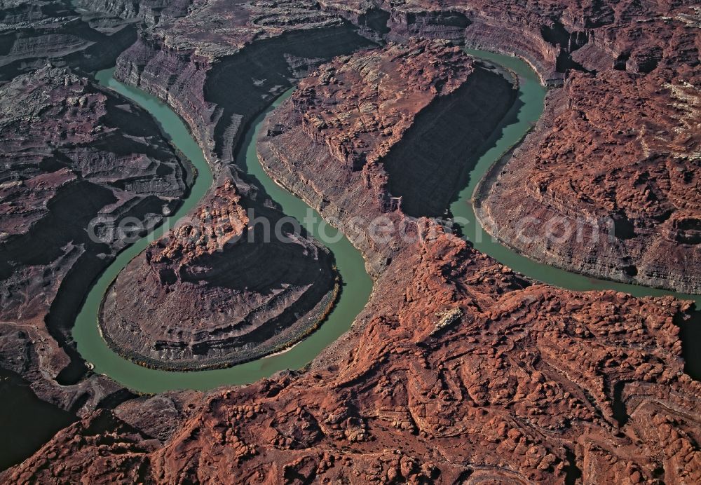 Aerial image Canyonlands National Park - Rock and mountain landscape with Colorado River in Canyonlands National Park in Utah, United States of America. Fine particles of mud and algae - suspended matter - gives the Colorado River its colour. Particularly when in full flow the river carries a lot of sand and rubble. This has allowed it to carve its mean ders deeper and deeper into the rock strata of the Colorado Plateau over tens of thousands of years