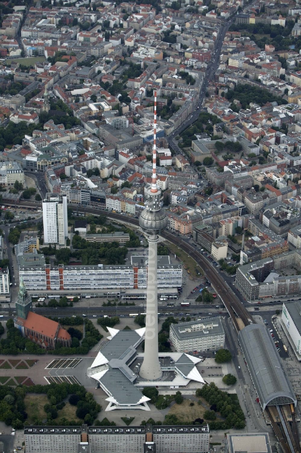 Aerial photograph Berlin - The TV tower at Alexanderplatz in Berlin in the state of Berlin is one of the landmarks of the capital. In the ball under the radio mast is a viewing platform and a restaurant. At the foot of the television tower is the S-Bahn station Alexanderplatz. On the tracks of the rail the train reached the station Hackescher Markt. From the urban houses sea the spiers of the church of St. Sophia and St. Mary's Church stand out. Along the Rosenthaler Strasse and the Brunnen road the green spaces of Garnisions cementry and the Weinberg Park can be seen