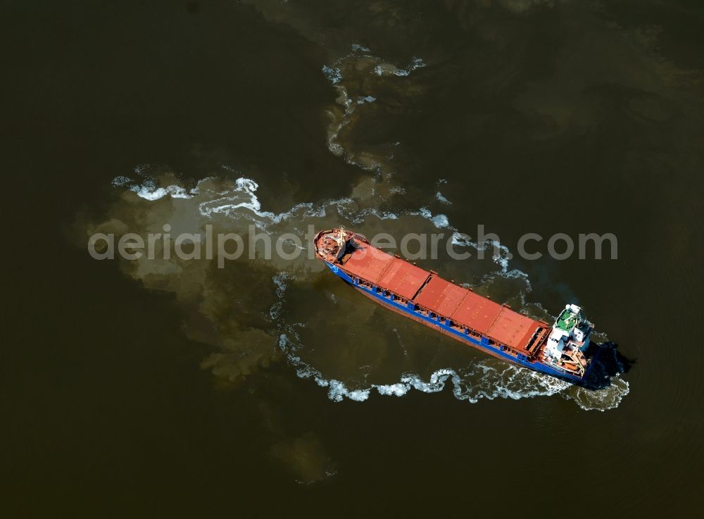 Emden from above - Freight ship in the Ems mouth in front of Emden in the state of Lower Saxony. The large freighter with its red deck is located iin front of the industrial port of Emden, where the river Ems connects to the North Sea