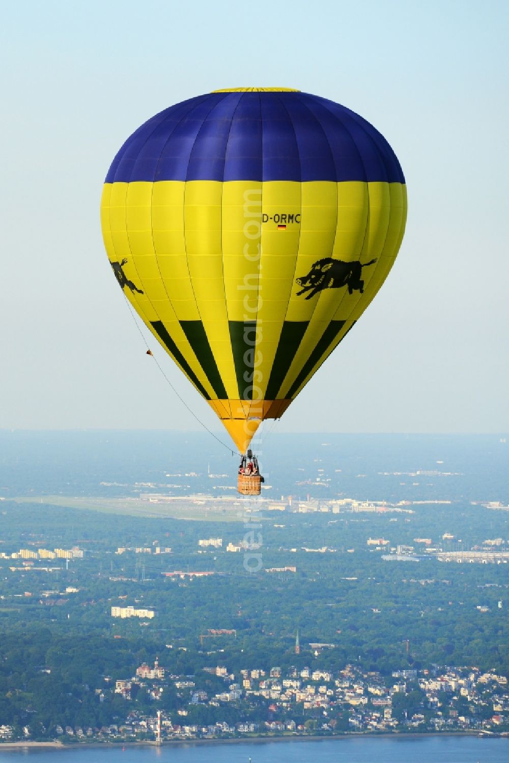 Jork from the bird's eye view: A yellow- blue coloured hot-air balloon with the identifier D-ORMC in flight above Jork in the state Lower Saxony