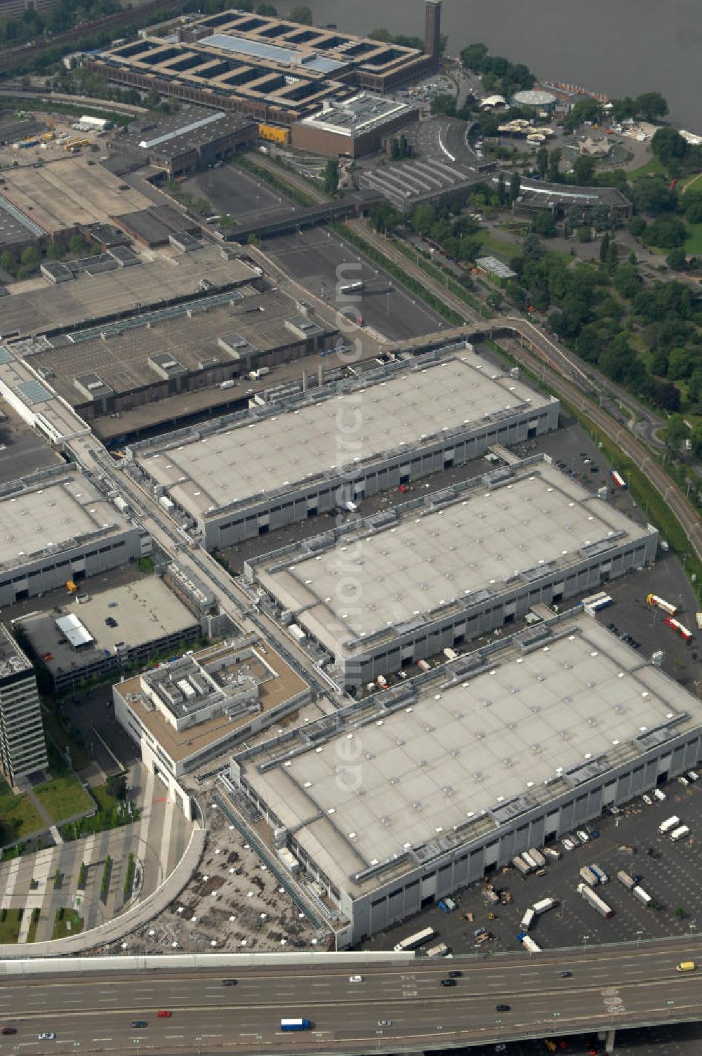 KÖLN from above - Blick auf das Gelände der Kölnmesse östlich des Rheins. Sie ist ein wichtiger Faktor für den Wirtschaft Kölns und den Wirtschaftsstandort Köln. Die Koelnmesse organisiert regelmäßig über 70 Messen im In- und Ausland. 25 davon gelten als die bedeutendsten Messen im jeweiligen Wirtschaftszweig. Somit ist die Koelnmesse größter Veranstalter von Messen auf einem eigenen Gelände und, gemessen an ihrer Ausstellungsfläche, die viert größte Messe weltweit. Jährlich werden rund 2,3 Millionen Besucher aus fast 200 Ländern gezählt. Das Gelände bietet Kapazitäten für Tagungen mit über 19.500 Teilnehmern und den Rahmen für Kongresse mit begleitenden Ausstellungen.