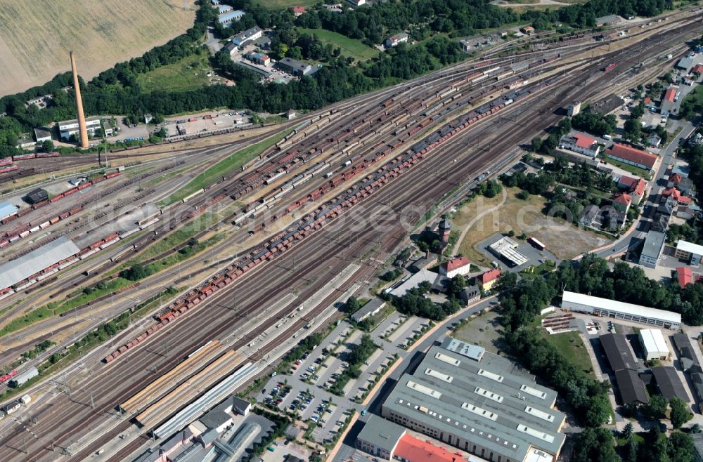 Aerial photograph Saalfeld/Saale - The train station of Saalfeld in Thuringia has a large freight yard. Countless tracks are available here for shunting. General freight cars waiting to be collected on new freight trains. In the background stands a chimney