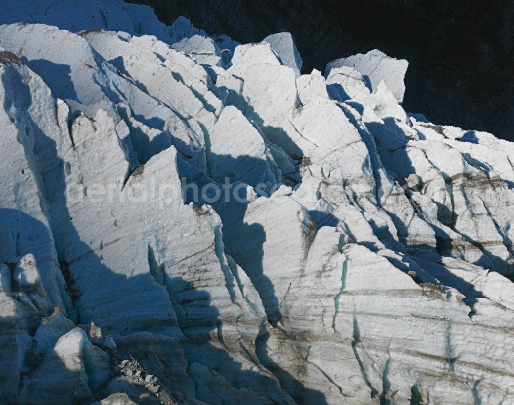 Saint-Gervais-les-Bains from above - Glaciers Bossons Glacier in the rock and mountain landscape in Saint-Gervais-les-Bains in Auvergne-Rhone-Alpes, France. Huge crevasses cut into the rim of the glacier tongue at the glacier front. Debris is imbedded in the ice seen as dark stripes in the steep melting ice walls