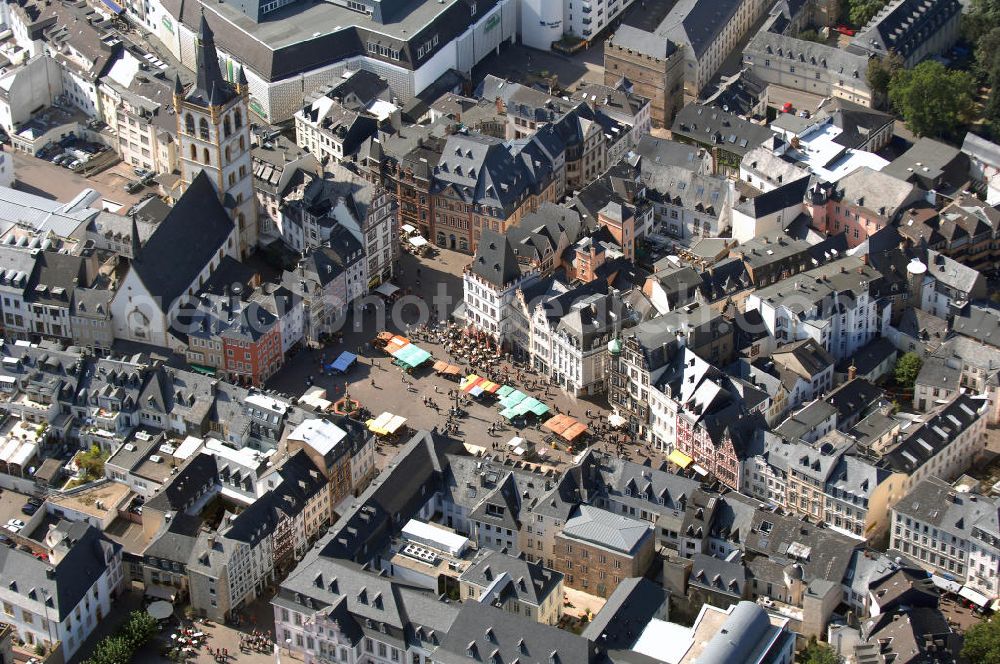 TRIER from above - Der Hauptmarkt von Trier ist der zentrale und einer der größten Plätze der Stadt.Er befindet sich im historischen Stadtkern unmittelbar vor der historischen Domstadt im heutigen Bezirk Mitte/Gartenfeld. Die wichtigsten städtischen Geschäftsstraßen treffen hier zusammen. Im Jahr 958 wurde der Hauptmarkt durch Erzbischof Heinrich I. mit dem Marktkreuz als Hoheitssymbol ausgestattet. Der Hauptmarkt diente der mittelalterlichen Stadt als Warenverkaufs- und Handelsplatz.Die historische Marktumbauung mit Häusern der Renaissance, des Barock, des Klassizismus und des Späthistorismus ist zu zwei Dritteln bewahrt. Prägend sind heute zahlreiche volumige und städtisch-repräsentative Gebäude, darunter etwa die Hauptwache oder das ehemalige Domhotel im Neorenaissance-Stil deutscher Prägung. Noch heute stehen dort außerdem die Steipe, ein um 1430 errichtetes Bürgerhaus und heute das Repräsentationshaus des Stadtrats sowie das Rote Haus mit dem Spruch über die sagenhafte Gründung Triers durch Trebeta. Die Kirche St. Gangolf ist nur über ein Barocktor vom Markt aus zugänglich und ansonsten komplett umbaut.