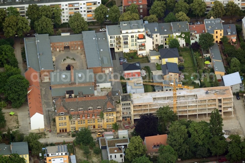 Aerial photograph Berlin - Historic factory and construction site of a new development amidst a residential area in the Friedrichshagen part of Berlin in Germany. The area is located between Ahornallee and Peter-Hille-Strasse and includes single and multi-family houses as well as the factory with the yellow main building and halls with a chimney. A construction site of a new development is sitting next to it