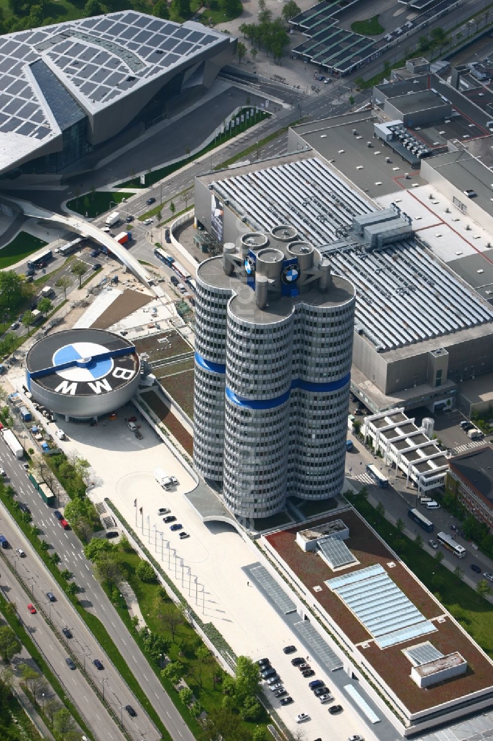 München from above - The skyscraper BMW Headquarters in Munich in Bavaria is part of the corporate headquarters of the car manufacturer BMW. The building consists of four office towers that are arranged as a four cylinder. Designed the BMW Tower by architect Karl Schwanzer. The rotunda with the BMW logo includes the BMW museum. The low-rise building in the background is the BMW world a combined exhibition, delivery, adventure, museum and event location. On the roof of the multifunctional building a solar power plant produces electricity. Architect of the building are Prof. Wolf D. Prix and the architectural firm Coop Himmelb (l) au