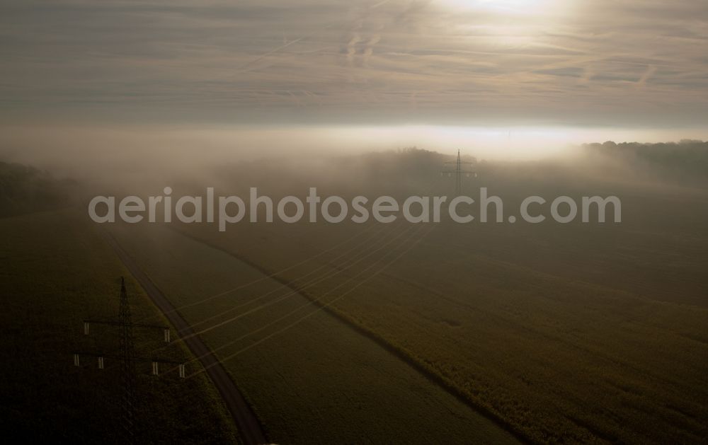 Mompach from the bird's eye view: Power lines and pylons in morning mist on a field in Mompach in Grevenmacher, Luxembourg