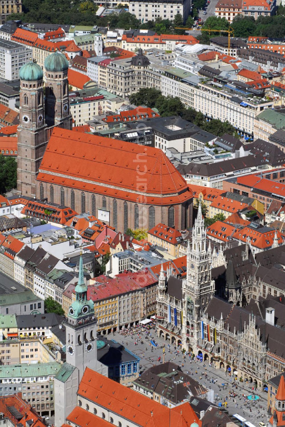 München from above - Innenstadt von München mit Blick auf die Frauenkirche, das Neue Rathaus und die Pfarrkirche St. Peter. Die Frauenkirche (Bildmitte) ist die Kathedralkirche des Erzbischofs von München und Freising und gilt als Wahrzeichen der bayerischen Landeshauptstadt. Der dreischiffige spätgotische Backsteinbau mit umlaufendem Kapellenkranz ist 109 m lang, 40 m breit und 37 m hoch. Die Grundsteinlegung für die heutige Frauenkirche erfolgte im Jahr 1468 durch Herzog Sigismund. Da man aus Kostengründen einen gemauerten Backsteinbau errichten wollte, statt auf teure Steinmetzarbeiten zurück zu greifen, wurde die Leitung der Bauarbeiten Jörg von Halspach, einem Maurermeister, übertragen. Im Jahr 1494 wurde die Frauenkirche geweiht. Im Zweiten Weltkrieg schwer beschädigt, wurde die Kirche in der Nachkriegszeit wieder aufgebaut, dabei erhielt sie ihr heutiges eher nüchternes, aber dennoch gewaltiges und markantes Äußeres. Von der ursprünglichen Ausstattung sind noch einige mittelalterliche Skulpturen und die mittelalterlichen Glasgemälde der Chorfenster erhalten geblieben. Mit ihrer herrlichen zentralen Lage inmitten einer großzügigen Fußgängerzone, die zwischen Karlsplatz und Marienplatz eingerichtet wurde, ist die Frauenkirche eine der meistbesuchtesten Sehenswürdigkeiten Münchens. Kontakt: Dom Zu Unserer Lieben Frau, Frauenplatz 12, 80331 München, Tel.: 089/290082-0, E-Mail: dompfarramt@muenchner-dom.de,