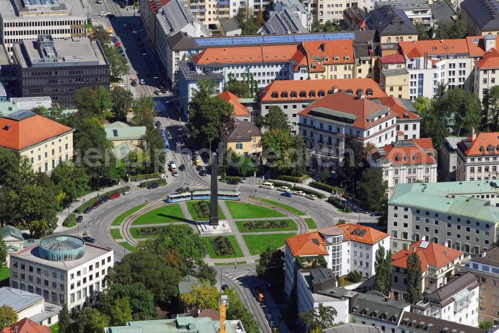 München from above - Blick auf den Karolinenplatz in München. Der Karolinenplatz ist ein öffentlicher Platz im Münchner Stadtteil Maxvorstadt. Er ist der erste Platz in München, der das Motiv des Strahlenplatzes aufgreift. Gleichzeitig will der Karolinenplatz die Entwicklung der besonderen Beziehung zwischen Bayern und Frankreich im 19. Jh. symbolisieren. Die Geschichte des Karolinenplatzes ist eng mit der Brienner Straße verknüpft. Bereits in einem städtebaulichen Wettbewerb von 1807 für die Maxvorstadt, aus dem der Plan für ein hippodamisch organisiertes Viertel hervorgeht, war ein Platz am alten wittelsbachischen Fürstenweg von der Münchner Residenz zum Schloss Nymphenburg, der heutigen Brienner Straße, an der Stelle des heutigen Karolinenplatz vorgesehen. Die Geschichte Bayerns ist eng mit der Frankreichs verknüpft. Brienner Straße und Barer Straße sind nach Orten von Schlachten des Deutsch-Französischer Krieges 1870/71 benannt, an deren siegreichem Ausgang bayerische Truppen besonderen Anteil hatten. Auf dem Schnittpunkt der beiden Straßen der „großen Siege“ steht der von Klenze 1833 errichtete, 29 m hohe Obelisk, der an die 30.000 bayerischen Gefallenen des Rußlandfeldzuges Napoléons erinnert. Somit sind Anfang und Ende dieser besonderen Beziehung zwischen München und Napoléon und seinen Nachfolgern im Schnittpunkt vereint. Im Zweiten Weltkrieg schwer beschädigt, ist der Karolinenplatz heute weitgehend von Neubauten geprägt, die den klassizistischen Eindruck nicht wiederherstellen.