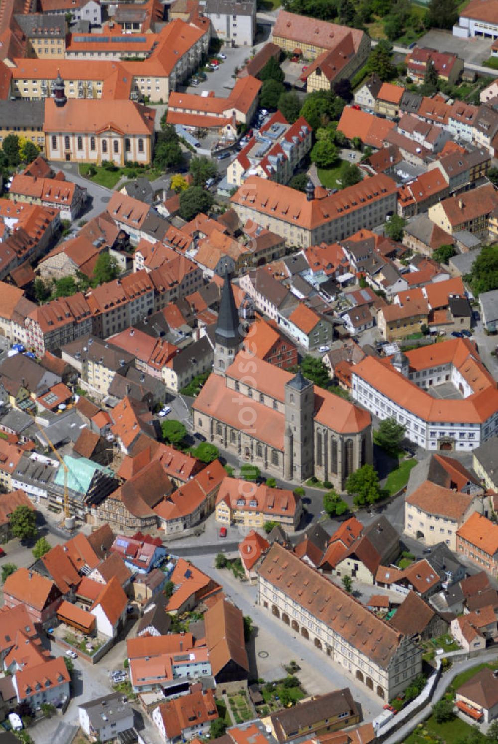 Aerial image Münnerstadt - Blick auf die Stadtpfarrkirche Münnerstadt. Die Katholische Stadtpfarrkirche St. Maria Magdalena entstand um 1230 im spätromanischen Stil dreischiffig. Zu Beginn des 15. Jh. leiteten die Ordensritter den Umbau im gotischen Stil ein. Heute bekannt für den 1428 bis 1446 errichteten Hochaltar mit Glasmalereien und dem Magdalenaltar mit Riemenschneiderskulpturen von 1492. 1610 läßt Fürstbischof Julius Echter das Haupt- und die beiden Seitenschiffe zu einer mächtigen Renaissancehalle umbauen. Historisch besonders Wertvoll sind die vier 1503 von Veit Stoß geschaffenen Bildtalfeln der Klianslegende und die gotische Tafel Marientod sowie die 18 Zunftstangen (1680-1830) im Hochchor.