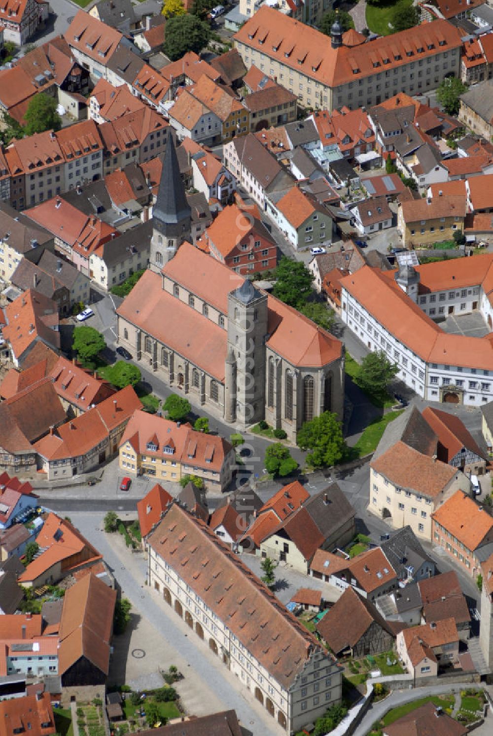 Münnerstadt from above - Blick auf die Stadtpfarrkirche Münnerstadt. Die Katholische Stadtpfarrkirche St. Maria Magdalena entstand um 1230 im spätromanischen Stil dreischiffig. Zu Beginn des 15. Jh. leiteten die Ordensritter den Umbau im gotichen Stil ein. Heute bekannt für den 1428 bis 1446 errichteten Hochaltar mit Glasmalereien und dem Magdalenaltar mit Riemenschneiderskulpturen von 1492. 1610 lässt Fürstbischof Julius Echter das Haupt- und die beiden Seitenschiffe zu einer mächtigen Renaissancehalle umbauen. Historisch besonders Wertvoll sind die vier 1503 von Veit Stoß geschaffenen Bildtalfeln der Klianslegende und die gotische Tafel Marientod sowie die 18 Zunftstangen (1680-1830) im Hochchor.