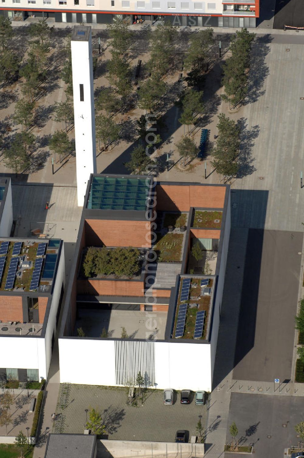 München from above - Das Kirchenzentrum Riem ist die räumliche wie auch geistige Mitte der 556 Hektar großen Messestadt Riem auf dem ehemaligen Flughafenbgelände ist das Kirchenzentrum der beiden großen christlichen Konfessionen am Platz der Menschenrechte. Die Pfarrerswohnung, die sich mit insgesamt fünf Zimmern auf zwei Ebenen über den Gemeinderäumen für Mutter und Kind erstreckt, orientiert sich nicht nur nach Süden auf einen großen Innenhof mit Bäumen. Vom ersten Obergeschoss des Pfarrhauses führt auch ein langer Holzsteg zu zwei Dachterrassen, die sich für Wolfgang Gerbere wie für kirchliche Zwecke nutzen lassen. Allein schon dieser Bereich des Kirchenzentrums vermittelt die städtebauliche Grundidee von Architekt Florian Nagler: Die ganze Anlage richtet sich nach innen auf vier unterschiedlich dimensionierte Höfe, die von hohen Wänden mit einem präzisen Fugenbild geschützt sind. Konsequenterweise hat Nagler mehrere Flachdächer für Veranstaltungen im Freien aktiviert.