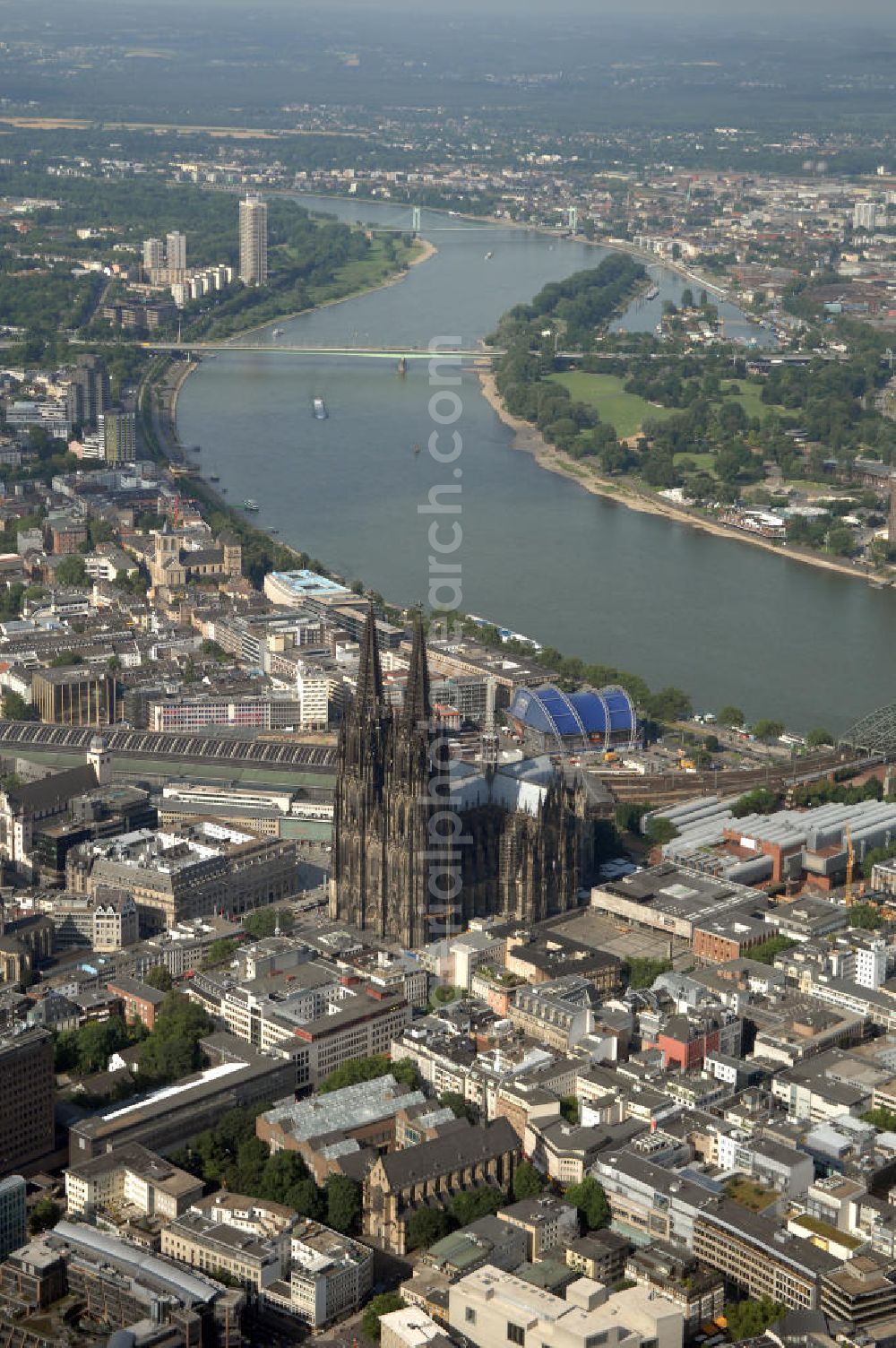 Aerial image KÖLN - Der Kölner Dom, offizieller Name Hohe Domkirche St. Peter und Maria, ist eine römisch-katholische Kirche in Köln und die Kathedrale des Erzbistums Köln.Der Kölner Dom ist mit 157 Metern Höhe nach dem Ulmer Münster die zweithöchste Kirche in Deutschland sowie die dritthöchste der Welt. Er steht an der nördlichen ehemaligen römischen Stadtgrenze in direkter Nachbarschaft des heutigen Hauptbahnhofs, der Altstadt, Hohenzollernbrücke und Museum Ludwig und ist von einer modernen Betonkonstruktion, der sogenannten Domplatte, umgeben. Vom rund 250 Meter entfernten Rhein und vom Hauptbahnhof aus ist die Lage der Kathedrale auf dem sogenannten Domhügel, rund 17 m über dem Rhein, noch zu erahnen. Der Kölner Dom ist die weltweit drittgrößte Kathedrale im gotischen Baustil (nach der Kathedrale von Sevilla und dem Mailänder Dom). Viele Kunsthistoriker sehen in ihm eine einmalige Harmonisierung sämtlicher Bauelemente und des Schmuckwerks im Stil der mittelalterlich-gotischen Architektur verwirklicht. Der Kölner Dom wurde 1996 in die Liste des Weltkulturerbes aufgenommen. Die riesige Fläche der Westfassade mitsamt den beiden Türmen von über 7.100 Quadratmetern ist bis heute nirgendwo übertroffen worden. Von 1880 bis 1884 war er das höchste Gebäude der Welt. Er ist zudem die populärste Sehenswürdigkeit Deutschlands: 2001 wurden fünf Millionen, 2004 sechs Millionen Besucher aus aller Welt gezählt.