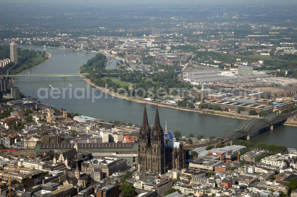 Aerial photograph KÖLN - Der Kölner Dom, offizieller Name Hohe Domkirche St. Peter und Maria, ist eine römisch-katholische Kirche in Köln und die Kathedrale des Erzbistums Köln.Der Kölner Dom ist mit 157 Metern Höhe nach dem Ulmer Münster die zweithöchste Kirche in Deutschland sowie die dritthöchste der Welt. Er steht an der nördlichen ehemaligen römischen Stadtgrenze in direkter Nachbarschaft des heutigen Hauptbahnhofs, der Altstadt, Hohenzollernbrücke und Museum Ludwig und ist von einer modernen Betonkonstruktion, der sogenannten Domplatte, umgeben. Vom rund 250 Meter entfernten Rhein und vom Hauptbahnhof aus ist die Lage der Kathedrale auf dem sogenannten Domhügel, rund 17 m über dem Rhein, noch zu erahnen. Der Kölner Dom ist die weltweit drittgrößte Kathedrale im gotischen Baustil (nach der Kathedrale von Sevilla und dem Mailänder Dom). Viele Kunsthistoriker sehen in ihm eine einmalige Harmonisierung sämtlicher Bauelemente und des Schmuckwerks im Stil der mittelalterlich-gotischen Architektur verwirklicht. Der Kölner Dom wurde 1996 in die Liste des Weltkulturerbes aufgenommen. Die riesige Fläche der Westfassade mitsamt den beiden Türmen von über 7.100 Quadratmetern ist bis heute nirgendwo übertroffen worden. Von 1880 bis 1884 war er das höchste Gebäude der Welt. Er ist zudem die populärste Sehenswürdigkeit Deutschlands: 2001 wurden fünf Millionen, 2004 sechs Millionen Besucher aus aller Welt gezählt.