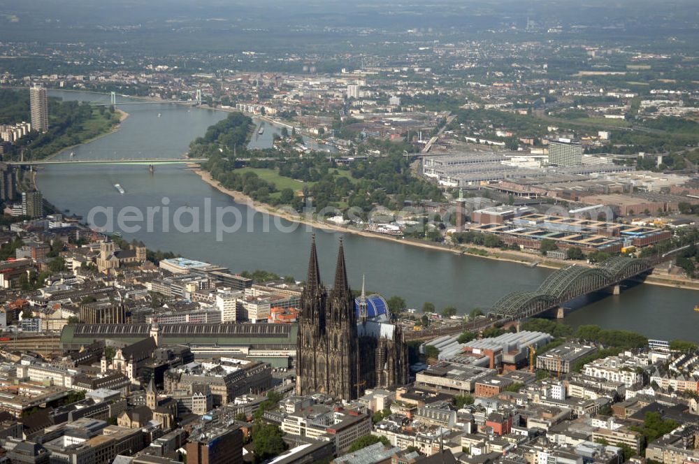 KÖLN from above - Der Kölner Dom, offizieller Name Hohe Domkirche St. Peter und Maria, ist eine römisch-katholische Kirche in Köln und die Kathedrale des Erzbistums Köln.Der Kölner Dom ist mit 157 Metern Höhe nach dem Ulmer Münster die zweithöchste Kirche in Deutschland sowie die dritthöchste der Welt. Er steht an der nördlichen ehemaligen römischen Stadtgrenze in direkter Nachbarschaft des heutigen Hauptbahnhofs, der Altstadt, Hohenzollernbrücke und Museum Ludwig und ist von einer modernen Betonkonstruktion, der sogenannten Domplatte, umgeben. Vom rund 250 Meter entfernten Rhein und vom Hauptbahnhof aus ist die Lage der Kathedrale auf dem sogenannten Domhügel, rund 17 m über dem Rhein, noch zu erahnen. Der Kölner Dom ist die weltweit drittgrößte Kathedrale im gotischen Baustil (nach der Kathedrale von Sevilla und dem Mailänder Dom). Viele Kunsthistoriker sehen in ihm eine einmalige Harmonisierung sämtlicher Bauelemente und des Schmuckwerks im Stil der mittelalterlich-gotischen Architektur verwirklicht. Der Kölner Dom wurde 1996 in die Liste des Weltkulturerbes aufgenommen. Die riesige Fläche der Westfassade mitsamt den beiden Türmen von über 7.100 Quadratmetern ist bis heute nirgendwo übertroffen worden. Von 1880 bis 1884 war er das höchste Gebäude der Welt. Er ist zudem die populärste Sehenswürdigkeit Deutschlands: 2001 wurden fünf Millionen, 2004 sechs Millionen Besucher aus aller Welt gezählt.