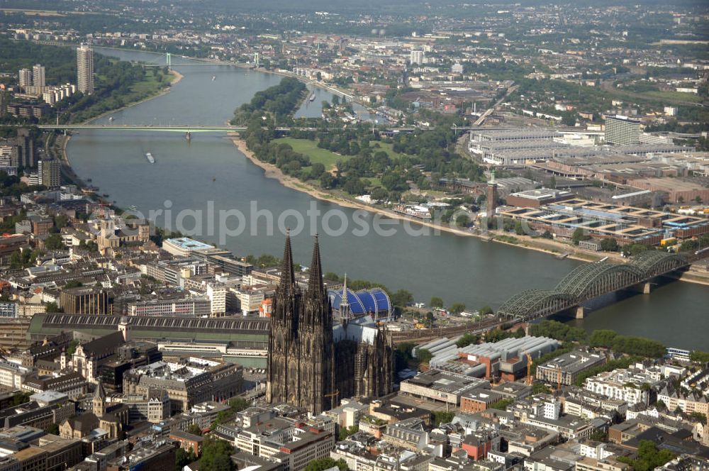 KÖLN from the bird's eye view: Der Kölner Dom, offizieller Name Hohe Domkirche St. Peter und Maria, ist eine römisch-katholische Kirche in Köln und die Kathedrale des Erzbistums Köln.Der Kölner Dom ist mit 157 Metern Höhe nach dem Ulmer Münster die zweithöchste Kirche in Deutschland sowie die dritthöchste der Welt. Er steht an der nördlichen ehemaligen römischen Stadtgrenze in direkter Nachbarschaft des heutigen Hauptbahnhofs, der Altstadt, Hohenzollernbrücke und Museum Ludwig und ist von einer modernen Betonkonstruktion, der sogenannten Domplatte, umgeben. Vom rund 250 Meter entfernten Rhein und vom Hauptbahnhof aus ist die Lage der Kathedrale auf dem sogenannten Domhügel, rund 17 m über dem Rhein, noch zu erahnen. Der Kölner Dom ist die weltweit drittgrößte Kathedrale im gotischen Baustil (nach der Kathedrale von Sevilla und dem Mailänder Dom). Viele Kunsthistoriker sehen in ihm eine einmalige Harmonisierung sämtlicher Bauelemente und des Schmuckwerks im Stil der mittelalterlich-gotischen Architektur verwirklicht. Der Kölner Dom wurde 1996 in die Liste des Weltkulturerbes aufgenommen. Die riesige Fläche der Westfassade mitsamt den beiden Türmen von über 7.100 Quadratmetern ist bis heute nirgendwo übertroffen worden. Von 1880 bis 1884 war er das höchste Gebäude der Welt. Er ist zudem die populärste Sehenswürdigkeit Deutschlands: 2001 wurden fünf Millionen, 2004 sechs Millionen Besucher aus aller Welt gezählt.