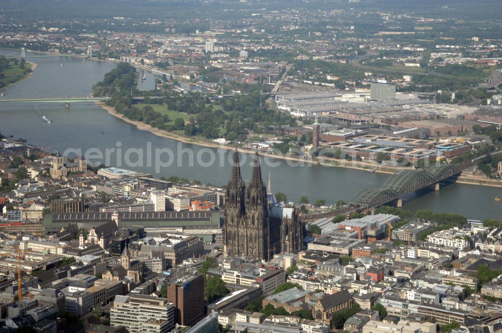 KÖLN from above - Der Kölner Dom, offizieller Name Hohe Domkirche St. Peter und Maria, ist eine römisch-katholische Kirche in Köln und die Kathedrale des Erzbistums Köln.Der Kölner Dom ist mit 157 Metern Höhe nach dem Ulmer Münster die zweithöchste Kirche in Deutschland sowie die dritthöchste der Welt. Er steht an der nördlichen ehemaligen römischen Stadtgrenze in direkter Nachbarschaft des heutigen Hauptbahnhofs, der Altstadt, Hohenzollernbrücke und Museum Ludwig und ist von einer modernen Betonkonstruktion, der sogenannten Domplatte, umgeben. Vom rund 250 Meter entfernten Rhein und vom Hauptbahnhof aus ist die Lage der Kathedrale auf dem sogenannten Domhügel, rund 17 m über dem Rhein, noch zu erahnen. Der Kölner Dom ist die weltweit drittgrößte Kathedrale im gotischen Baustil (nach der Kathedrale von Sevilla und dem Mailänder Dom). Viele Kunsthistoriker sehen in ihm eine einmalige Harmonisierung sämtlicher Bauelemente und des Schmuckwerks im Stil der mittelalterlich-gotischen Architektur verwirklicht. Der Kölner Dom wurde 1996 in die Liste des Weltkulturerbes aufgenommen. Die riesige Fläche der Westfassade mitsamt den beiden Türmen von über 7.100 Quadratmetern ist bis heute nirgendwo übertroffen worden. Von 1880 bis 1884 war er das höchste Gebäude der Welt. Er ist zudem die populärste Sehenswürdigkeit Deutschlands: 2001 wurden fünf Millionen, 2004 sechs Millionen Besucher aus aller Welt gezählt.