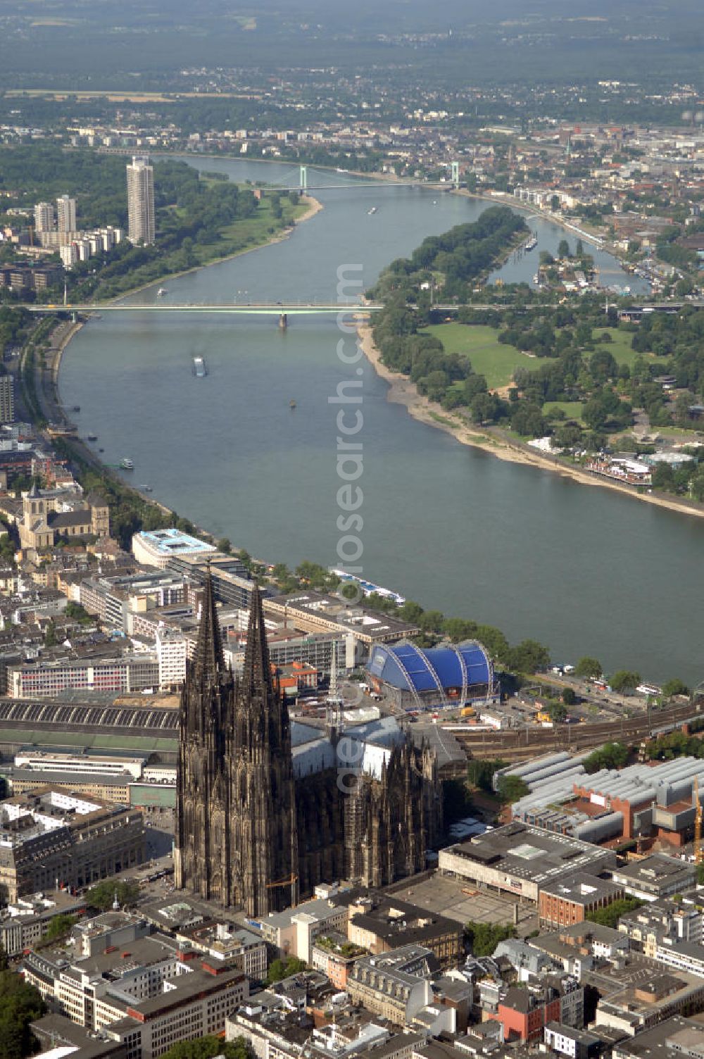 Aerial image KÖLN - Der Kölner Dom, offizieller Name Hohe Domkirche St. Peter und Maria, ist eine römisch-katholische Kirche in Köln und die Kathedrale des Erzbistums Köln.Der Kölner Dom ist mit 157 Metern Höhe nach dem Ulmer Münster die zweithöchste Kirche in Deutschland sowie die dritthöchste der Welt. Er steht an der nördlichen ehemaligen römischen Stadtgrenze in direkter Nachbarschaft des heutigen Hauptbahnhofs, der Altstadt, Hohenzollernbrücke und Museum Ludwig und ist von einer modernen Betonkonstruktion, der sogenannten Domplatte, umgeben. Vom rund 250 Meter entfernten Rhein und vom Hauptbahnhof aus ist die Lage der Kathedrale auf dem sogenannten Domhügel, rund 17 m über dem Rhein, noch zu erahnen. Der Kölner Dom ist die weltweit drittgrößte Kathedrale im gotischen Baustil (nach der Kathedrale von Sevilla und dem Mailänder Dom). Viele Kunsthistoriker sehen in ihm eine einmalige Harmonisierung sämtlicher Bauelemente und des Schmuckwerks im Stil der mittelalterlich-gotischen Architektur verwirklicht. Der Kölner Dom wurde 1996 in die Liste des Weltkulturerbes aufgenommen. Die riesige Fläche der Westfassade mitsamt den beiden Türmen von über 7.100 Quadratmetern ist bis heute nirgendwo übertroffen worden. Von 1880 bis 1884 war er das höchste Gebäude der Welt. Er ist zudem die populärste Sehenswürdigkeit Deutschlands: 2001 wurden fünf Millionen, 2004 sechs Millionen Besucher aus aller Welt gezählt.