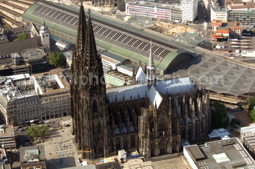 KÖLN from above - Der Kölner Dom, offizieller Name Hohe Domkirche St. Peter und Maria, ist eine römisch-katholische Kirche in Köln und die Kathedrale des Erzbistums Köln.Der Kölner Dom ist mit 157 Metern Höhe nach dem Ulmer Münster die zweithöchste Kirche in Deutschland sowie die dritthöchste der Welt. Er steht an der nördlichen ehemaligen römischen Stadtgrenze in direkter Nachbarschaft des heutigen Hauptbahnhofs, der Altstadt, Hohenzollernbrücke und Museum Ludwig und ist von einer modernen Betonkonstruktion, der sogenannten Domplatte, umgeben. Vom rund 250 Meter entfernten Rhein und vom Hauptbahnhof aus ist die Lage der Kathedrale auf dem sogenannten Domhügel, rund 17 m über dem Rhein, noch zu erahnen. Der Kölner Dom ist die weltweit drittgrößte Kathedrale im gotischen Baustil (nach der Kathedrale von Sevilla und dem Mailänder Dom). Viele Kunsthistoriker sehen in ihm eine einmalige Harmonisierung sämtlicher Bauelemente und des Schmuckwerks im Stil der mittelalterlich-gotischen Architektur verwirklicht. Der Kölner Dom wurde 1996 in die Liste des Weltkulturerbes aufgenommen. Die riesige Fläche der Westfassade mitsamt den beiden Türmen von über 7.100 Quadratmetern ist bis heute nirgendwo übertroffen worden. Von 1880 bis 1884 war er das höchste Gebäude der Welt. Er ist zudem die populärste Sehenswürdigkeit Deutschlands: 2001 wurden fünf Millionen, 2004 sechs Millionen Besucher aus aller Welt gezählt.