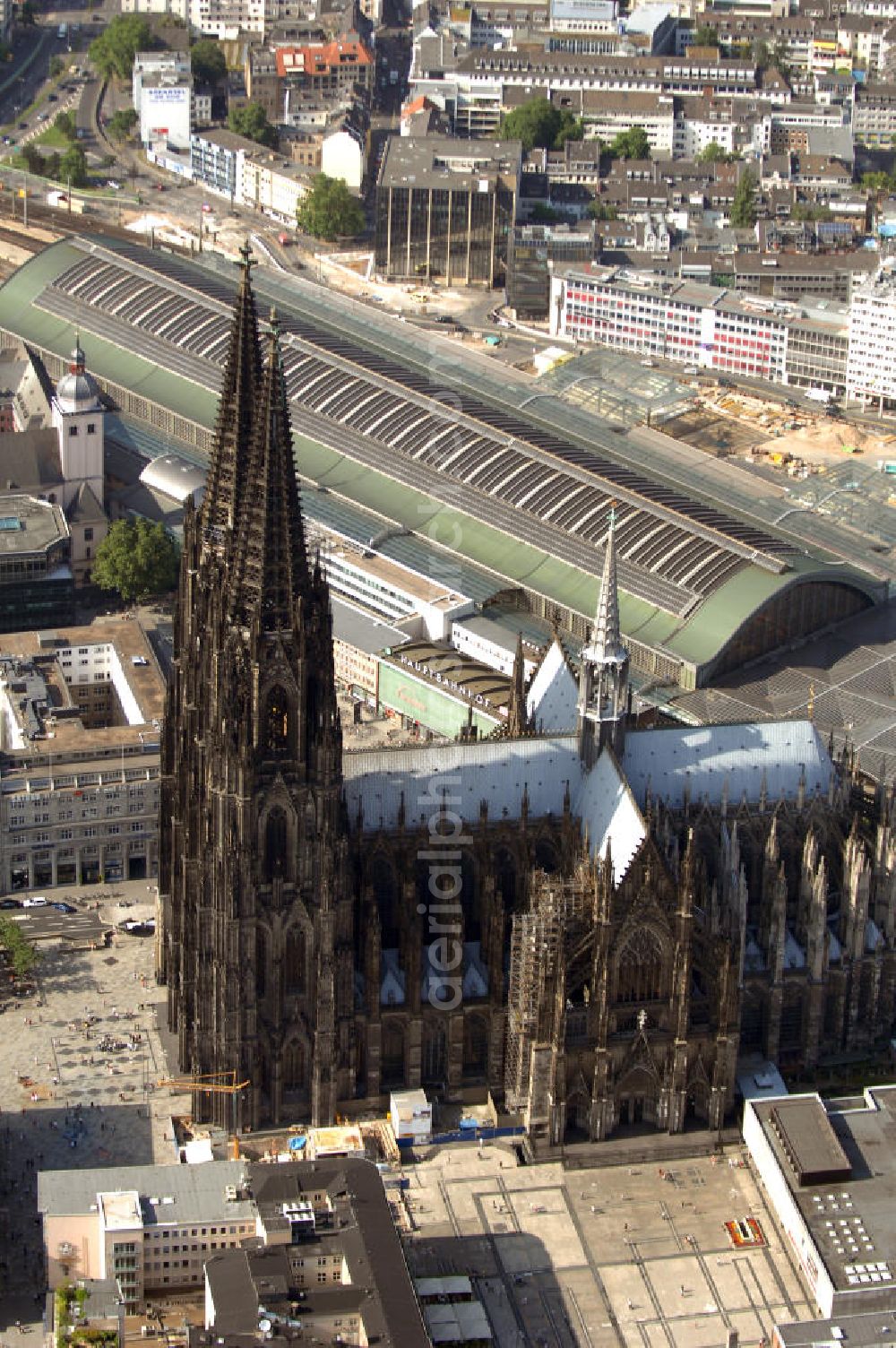 KÖLN from the bird's eye view: Der Kölner Dom, offizieller Name Hohe Domkirche St. Peter und Maria, ist eine römisch-katholische Kirche in Köln und die Kathedrale des Erzbistums Köln.Der Kölner Dom ist mit 157 Metern Höhe nach dem Ulmer Münster die zweithöchste Kirche in Deutschland sowie die dritthöchste der Welt. Er steht an der nördlichen ehemaligen römischen Stadtgrenze in direkter Nachbarschaft des heutigen Hauptbahnhofs, der Altstadt, Hohenzollernbrücke und Museum Ludwig und ist von einer modernen Betonkonstruktion, der sogenannten Domplatte, umgeben. Vom rund 250 Meter entfernten Rhein und vom Hauptbahnhof aus ist die Lage der Kathedrale auf dem sogenannten Domhügel, rund 17 m über dem Rhein, noch zu erahnen. Der Kölner Dom ist die weltweit drittgrößte Kathedrale im gotischen Baustil (nach der Kathedrale von Sevilla und dem Mailänder Dom). Viele Kunsthistoriker sehen in ihm eine einmalige Harmonisierung sämtlicher Bauelemente und des Schmuckwerks im Stil der mittelalterlich-gotischen Architektur verwirklicht. Der Kölner Dom wurde 1996 in die Liste des Weltkulturerbes aufgenommen. Die riesige Fläche der Westfassade mitsamt den beiden Türmen von über 7.100 Quadratmetern ist bis heute nirgendwo übertroffen worden. Von 1880 bis 1884 war er das höchste Gebäude der Welt. Er ist zudem die populärste Sehenswürdigkeit Deutschlands: 2001 wurden fünf Millionen, 2004 sechs Millionen Besucher aus aller Welt gezählt.