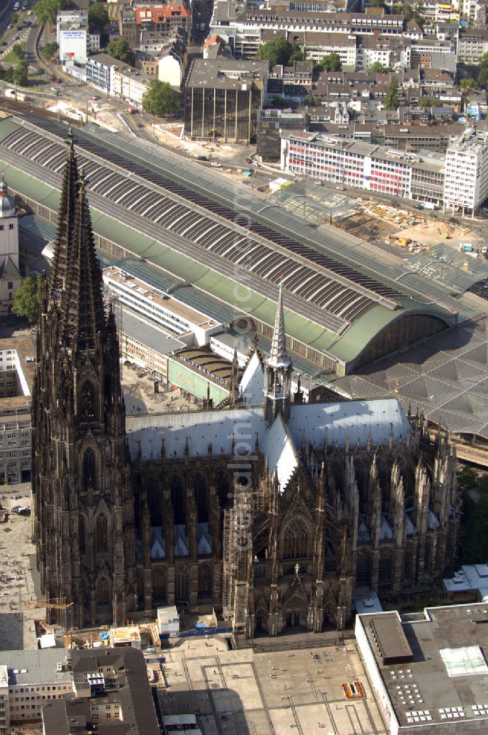 Aerial photograph KÖLN - Der Kölner Dom, offizieller Name Hohe Domkirche St. Peter und Maria, ist eine römisch-katholische Kirche in Köln und die Kathedrale des Erzbistums Köln.Der Kölner Dom ist mit 157 Metern Höhe nach dem Ulmer Münster die zweithöchste Kirche in Deutschland sowie die dritthöchste der Welt. Er steht an der nördlichen ehemaligen römischen Stadtgrenze in direkter Nachbarschaft des heutigen Hauptbahnhofs, der Altstadt, Hohenzollernbrücke und Museum Ludwig und ist von einer modernen Betonkonstruktion, der sogenannten Domplatte, umgeben. Vom rund 250 Meter entfernten Rhein und vom Hauptbahnhof aus ist die Lage der Kathedrale auf dem sogenannten Domhügel, rund 17 m über dem Rhein, noch zu erahnen. Der Kölner Dom ist die weltweit drittgrößte Kathedrale im gotischen Baustil (nach der Kathedrale von Sevilla und dem Mailänder Dom). Viele Kunsthistoriker sehen in ihm eine einmalige Harmonisierung sämtlicher Bauelemente und des Schmuckwerks im Stil der mittelalterlich-gotischen Architektur verwirklicht. Der Kölner Dom wurde 1996 in die Liste des Weltkulturerbes aufgenommen. Die riesige Fläche der Westfassade mitsamt den beiden Türmen von über 7.100 Quadratmetern ist bis heute nirgendwo übertroffen worden. Von 1880 bis 1884 war er das höchste Gebäude der Welt. Er ist zudem die populärste Sehenswürdigkeit Deutschlands: 2001 wurden fünf Millionen, 2004 sechs Millionen Besucher aus aller Welt gezählt.