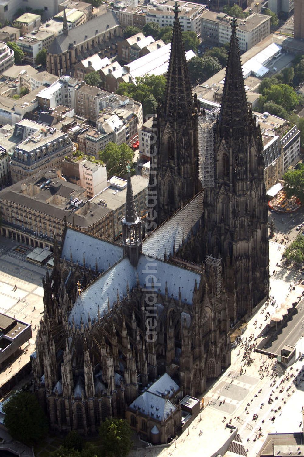 Aerial photograph KÖLN - Der Kölner Dom, offizieller Name Hohe Domkirche St. Peter und Maria, ist eine römisch-katholische Kirche in Köln und die Kathedrale des Erzbistums Köln.Der Kölner Dom ist mit 157 Metern Höhe nach dem Ulmer Münster die zweithöchste Kirche in Deutschland sowie die dritthöchste der Welt. Er steht an der nördlichen ehemaligen römischen Stadtgrenze in direkter Nachbarschaft des heutigen Hauptbahnhofs, der Altstadt, Hohenzollernbrücke und Museum Ludwig und ist von einer modernen Betonkonstruktion, der sogenannten Domplatte, umgeben. Vom rund 250 Meter entfernten Rhein und vom Hauptbahnhof aus ist die Lage der Kathedrale auf dem sogenannten Domhügel, rund 17 m über dem Rhein, noch zu erahnen. Der Kölner Dom ist die weltweit drittgrößte Kathedrale im gotischen Baustil (nach der Kathedrale von Sevilla und dem Mailänder Dom). Viele Kunsthistoriker sehen in ihm eine einmalige Harmonisierung sämtlicher Bauelemente und des Schmuckwerks im Stil der mittelalterlich-gotischen Architektur verwirklicht. Der Kölner Dom wurde 1996 in die Liste des Weltkulturerbes aufgenommen. Die riesige Fläche der Westfassade mitsamt den beiden Türmen von über 7.100 Quadratmetern ist bis heute nirgendwo übertroffen worden. Von 1880 bis 1884 war er das höchste Gebäude der Welt. Er ist zudem die populärste Sehenswürdigkeit Deutschlands: 2001 wurden fünf Millionen, 2004 sechs Millionen Besucher aus aller Welt gezählt.